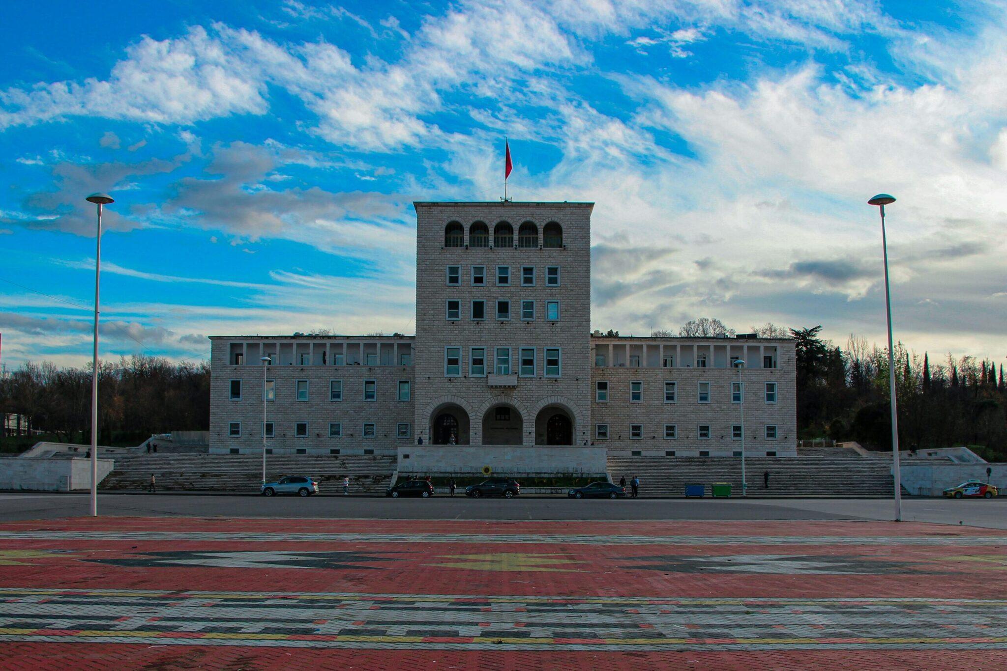 Un bâtiment gouvernemental blanc moderne avec drapeau national surplombant une vaste place pavée sous ciel bleu