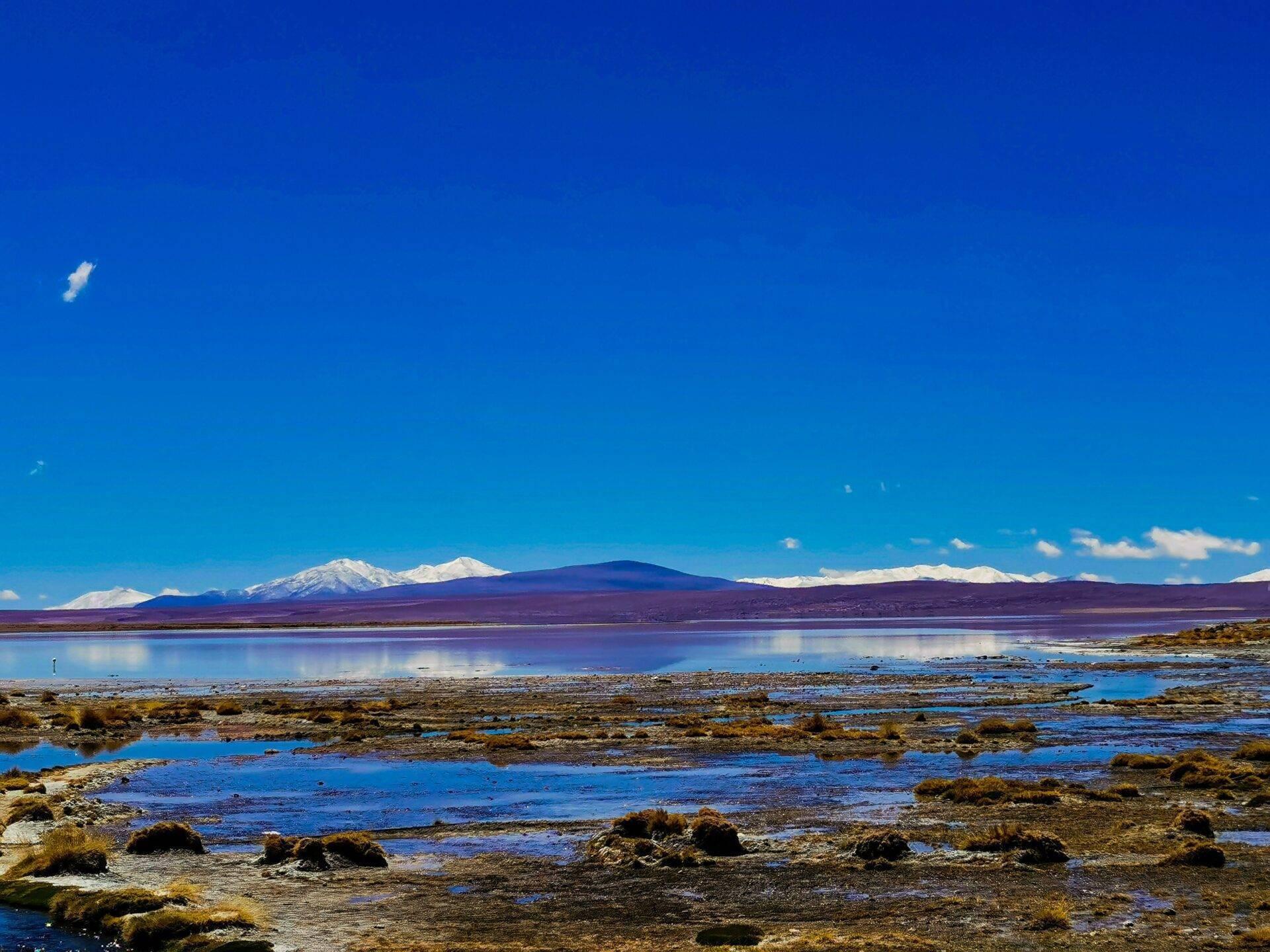 Paysage d’altitude avec lacs turquoise, formations rocheuses et volcans enneigés sous ciel bleu dégagé