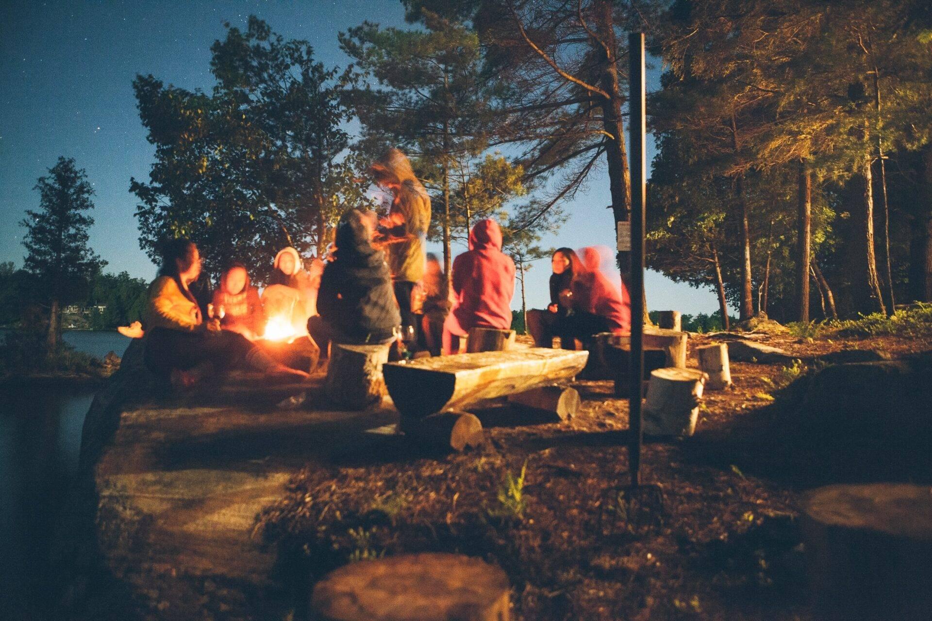 Groupe de personnes rassemblées autour d’un feu de camp en forêt lors d’une soirée hivernale