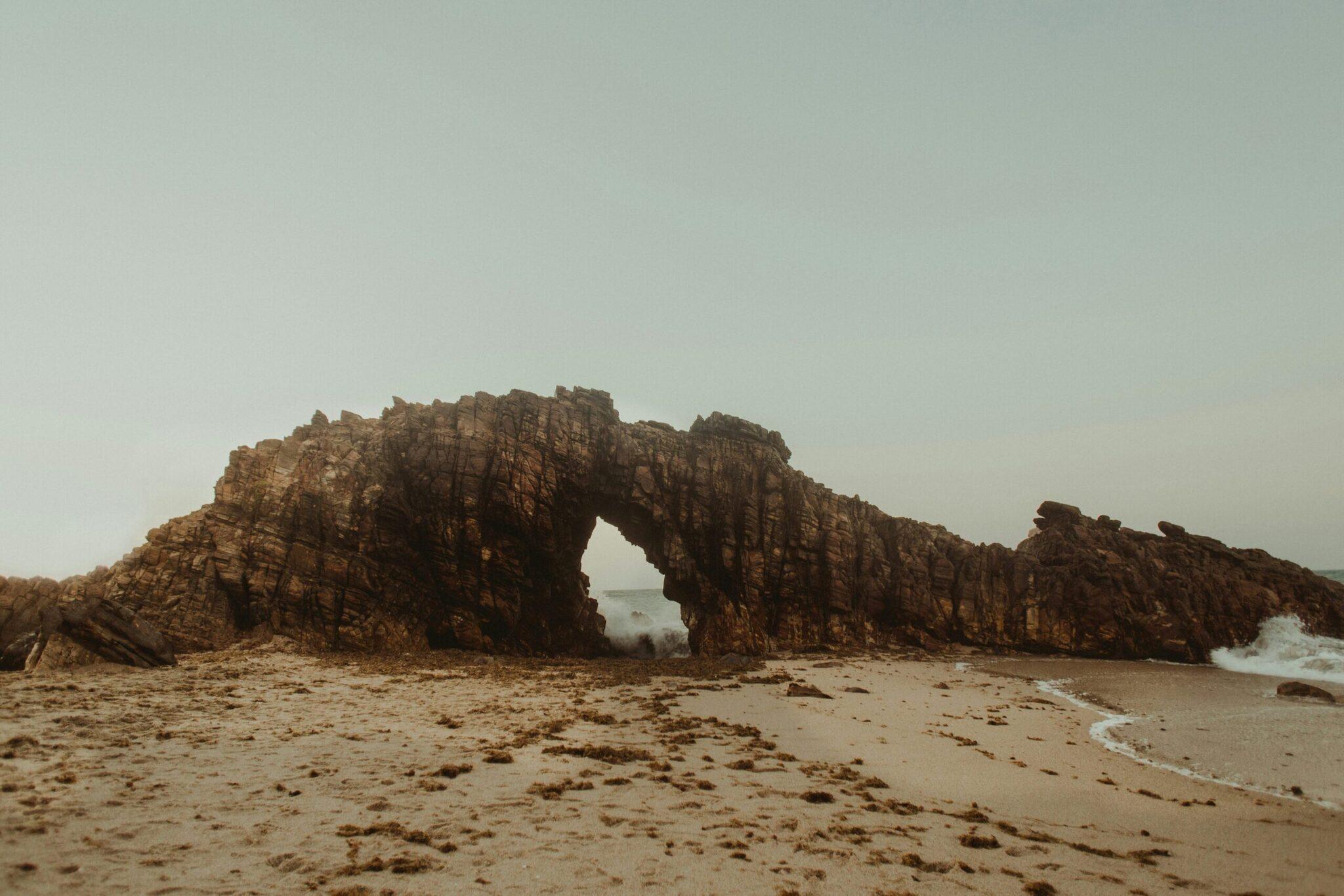 Une arche naturelle massive en roche érodée sur une plage déserte avec l’océan en arrière-plan