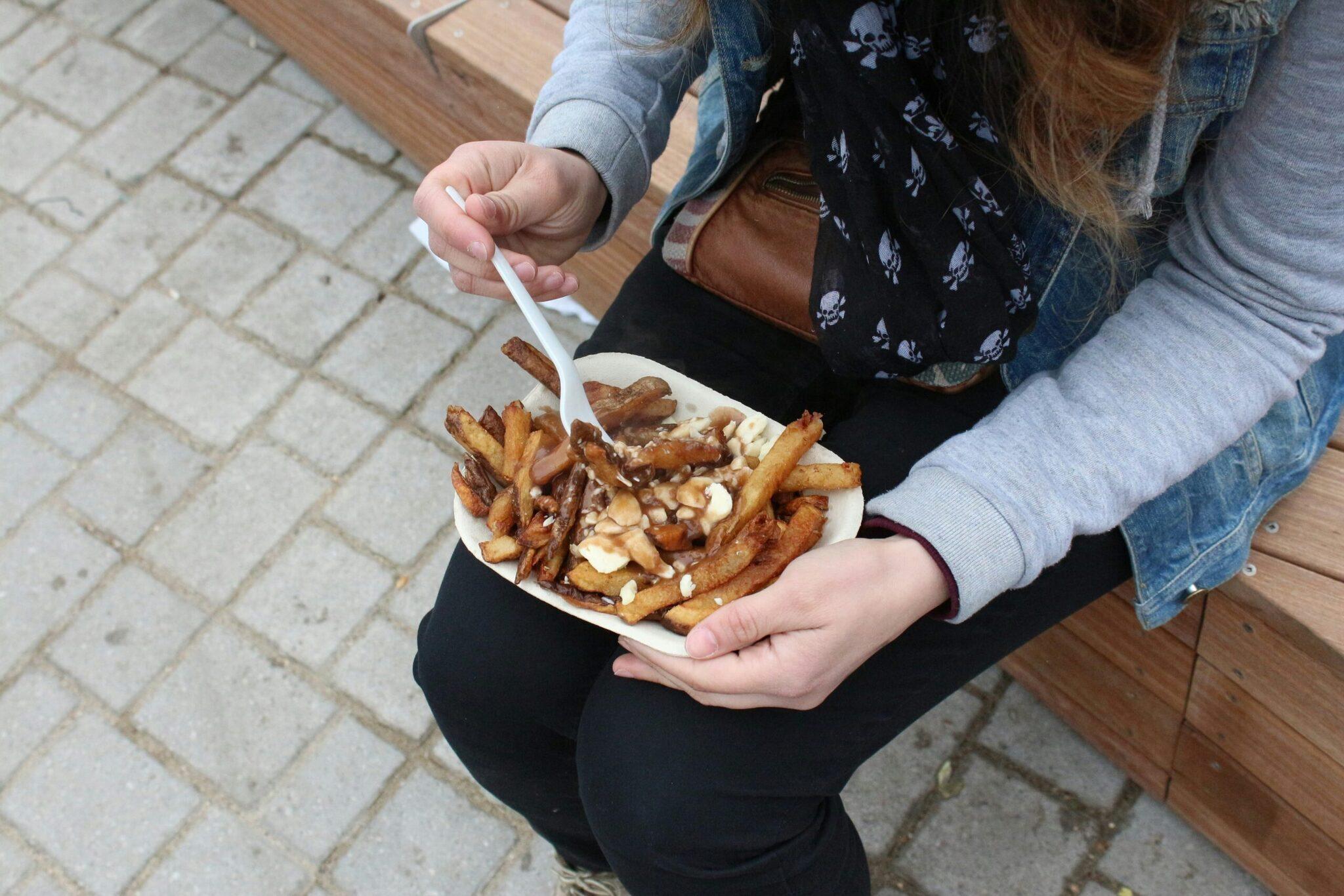Deux personnes dégustent des frites garnies de fromage en fromage sur une rue pavée de Montréal