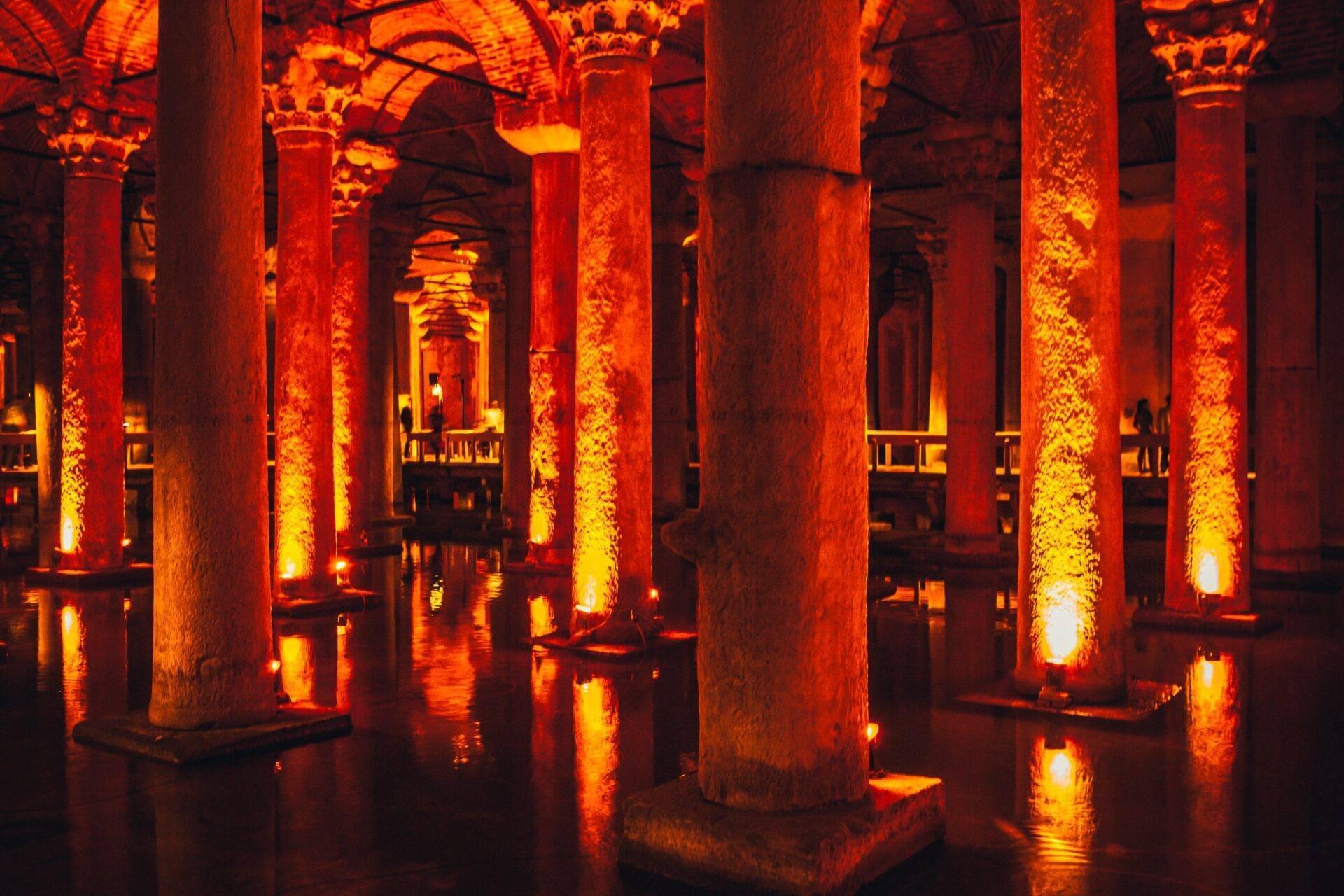 Une basilique souterraine illuminée en rouge-orange avec d’imposantes colonnes et leurs reflets dans l’eau