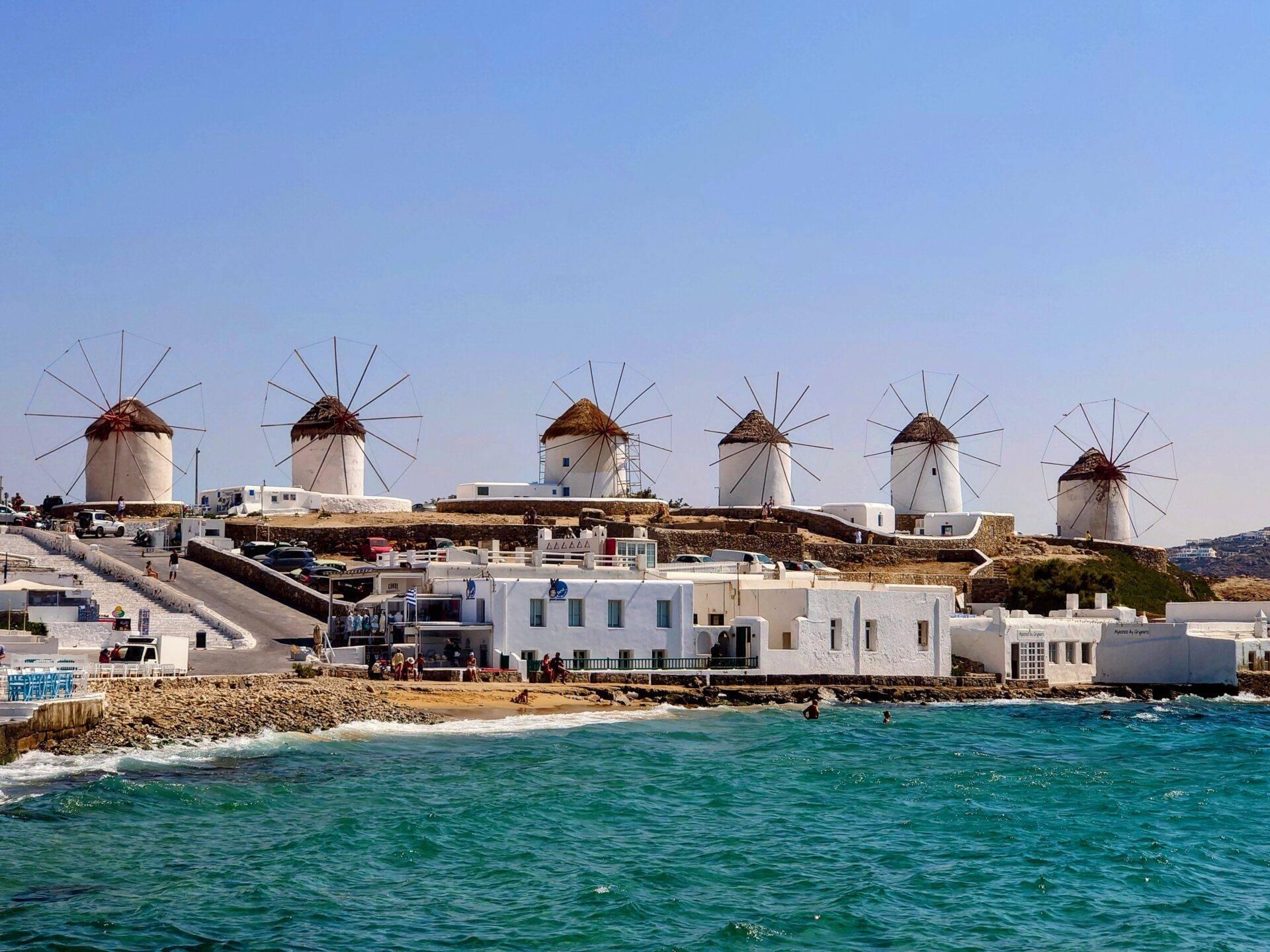 Six moulins à vent blancs traditionnels surplombant des maisons blanches et la mer turquoise en Méditerranée