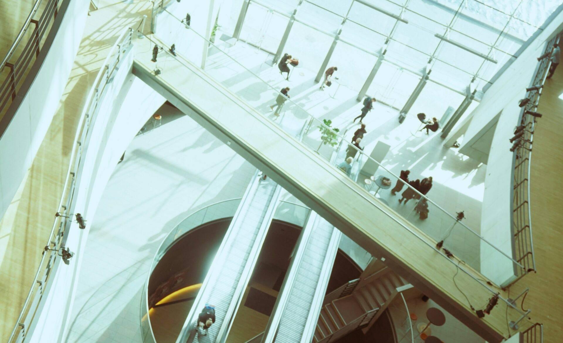 Vue plongeante d’un atrium moderne avec escaliers mécaniques et visiteurs circulant dans un espace architectural épuré et lumineux