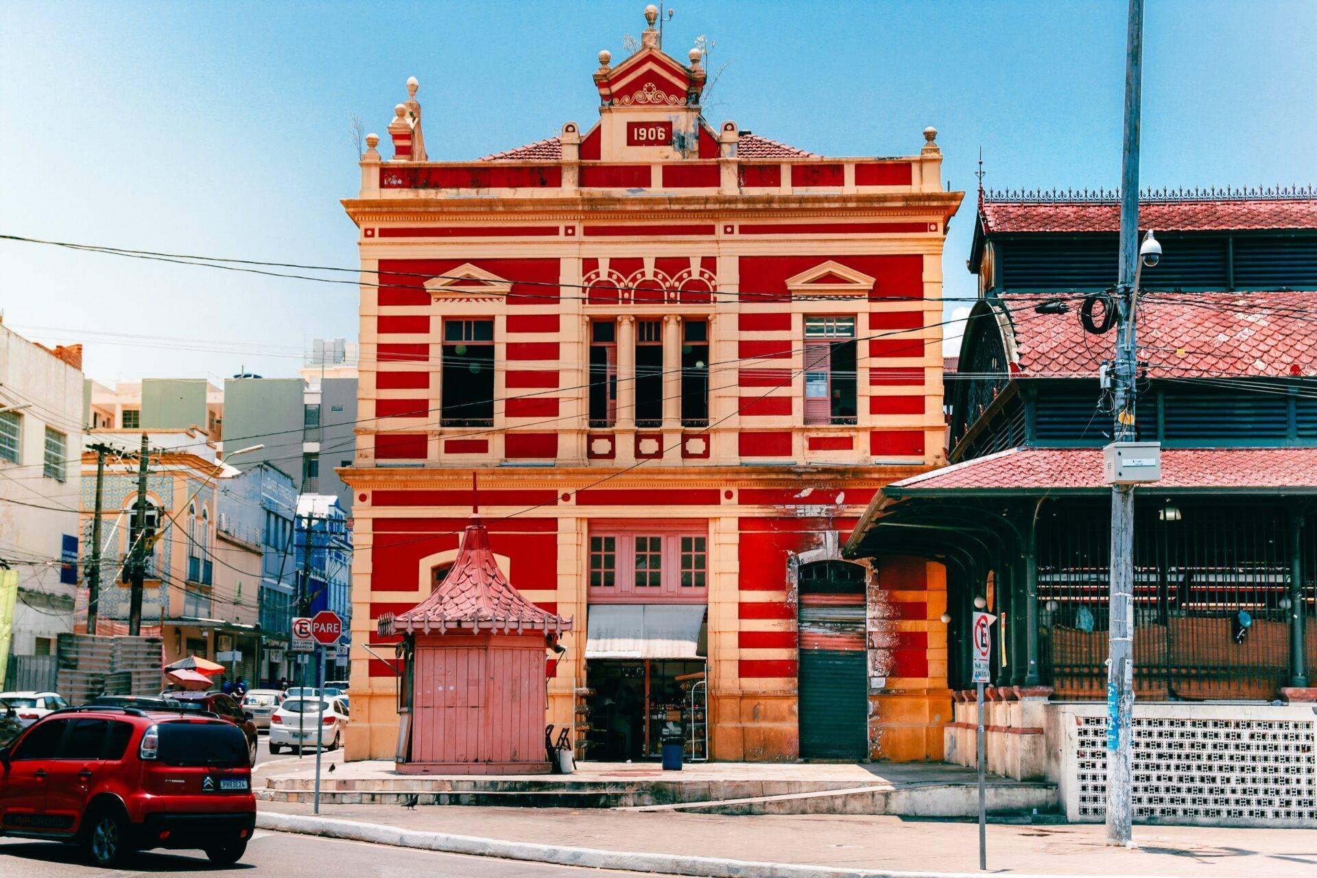 Bâtiment historique rouge et blanc datant de 1906 avec architecture coloniale, entouré de rues urbaines modernes