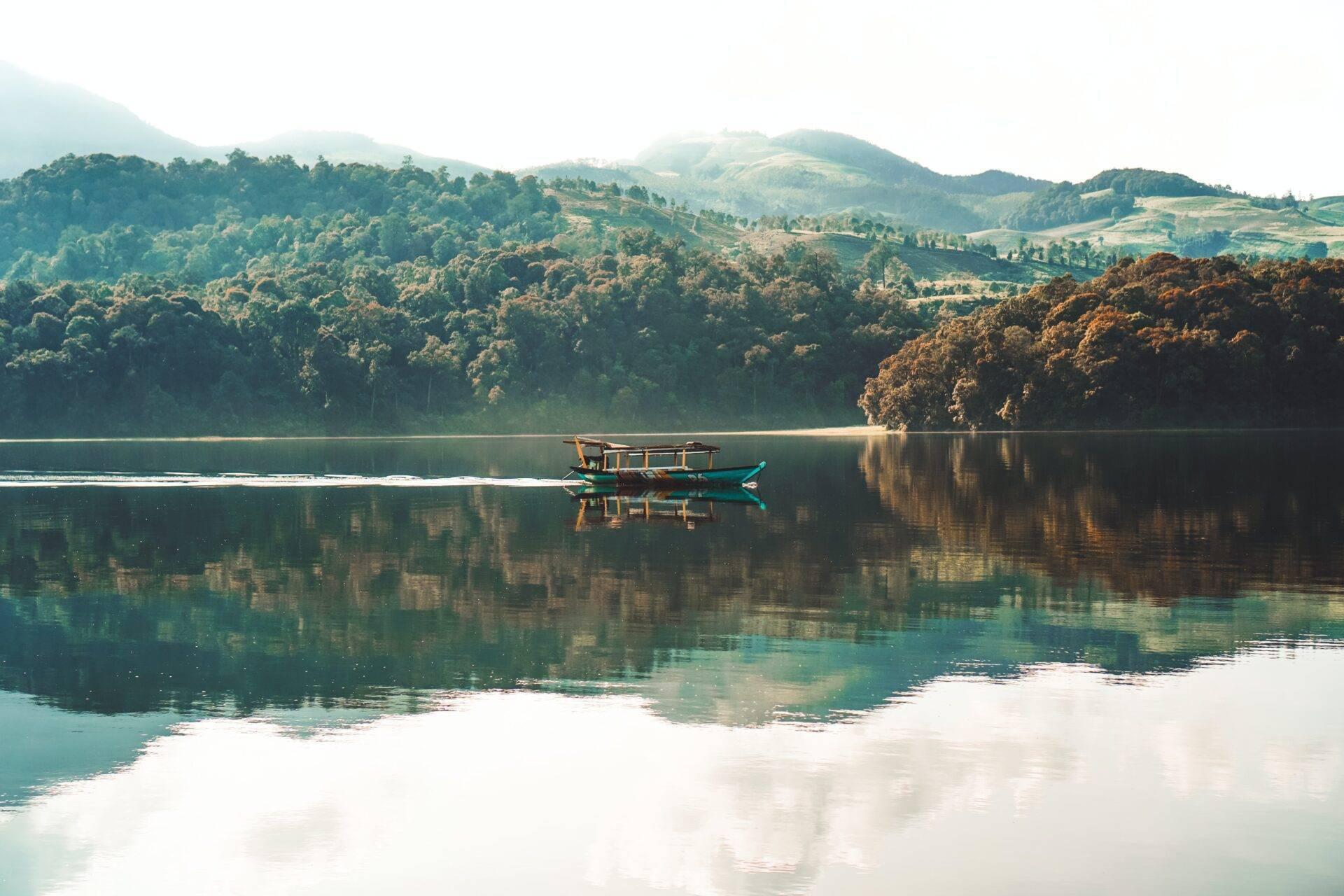 Un bateau de pêche traditionnel bleu sur un lac miroir entouré de montagnes boisées et de jungle verdoyante