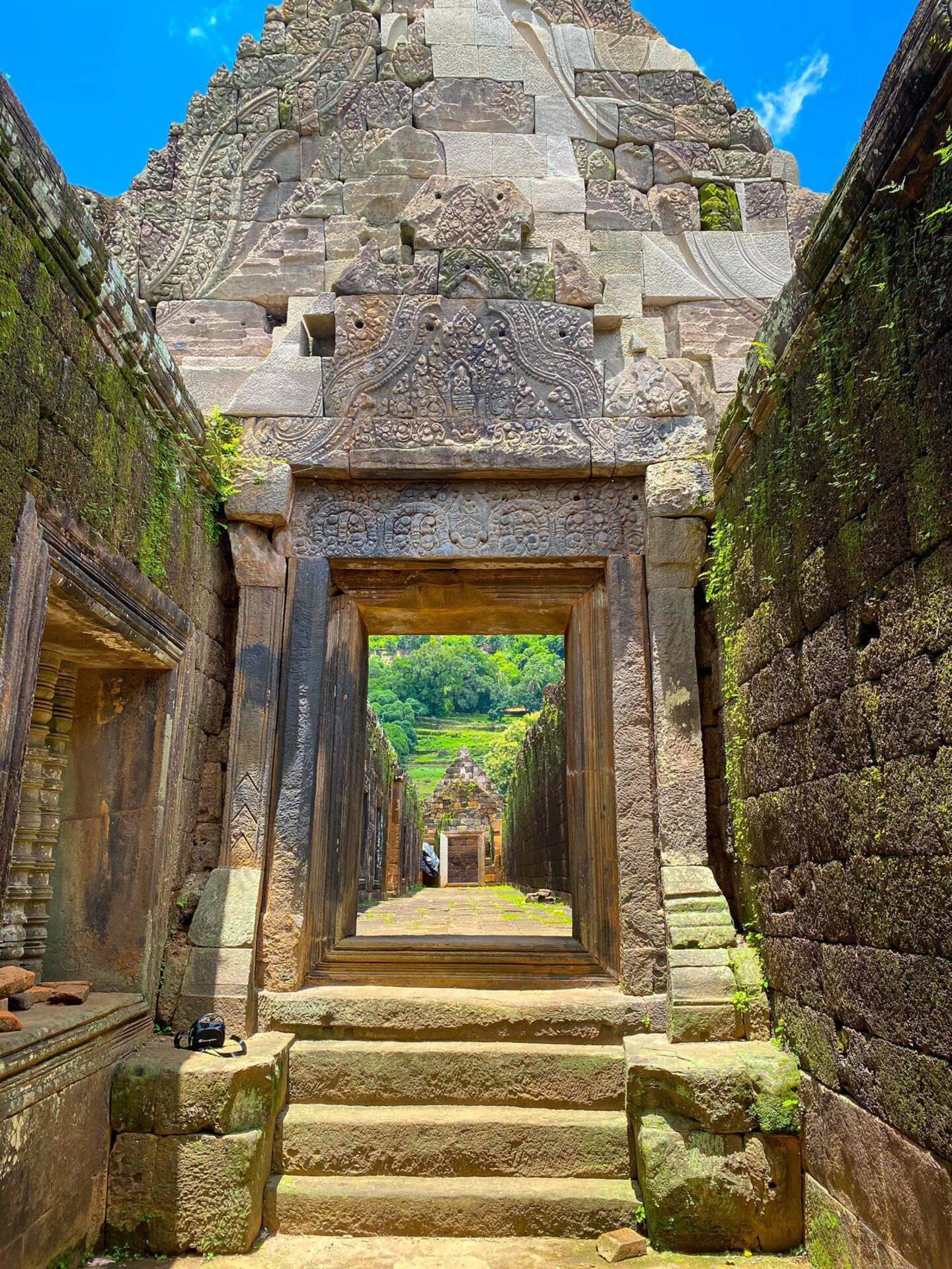 Vue en enfilade de portes ornementées d’un temple khmer ancien, avec jungle verdoyante visible au loin