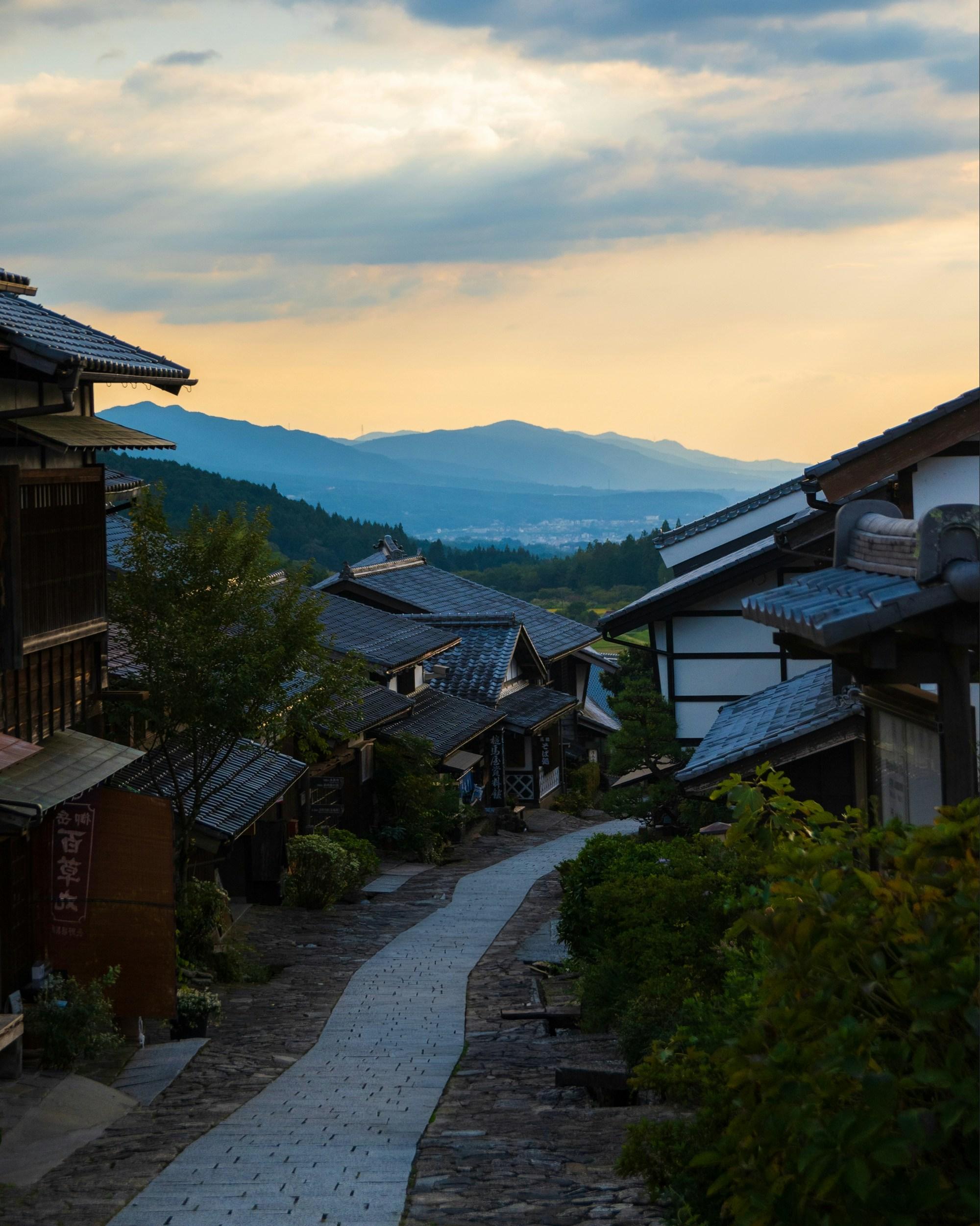Vue sur une vallée depuis une rue pavée bordée de maisons traditionnelles japonaises avec toits en tuiles noires