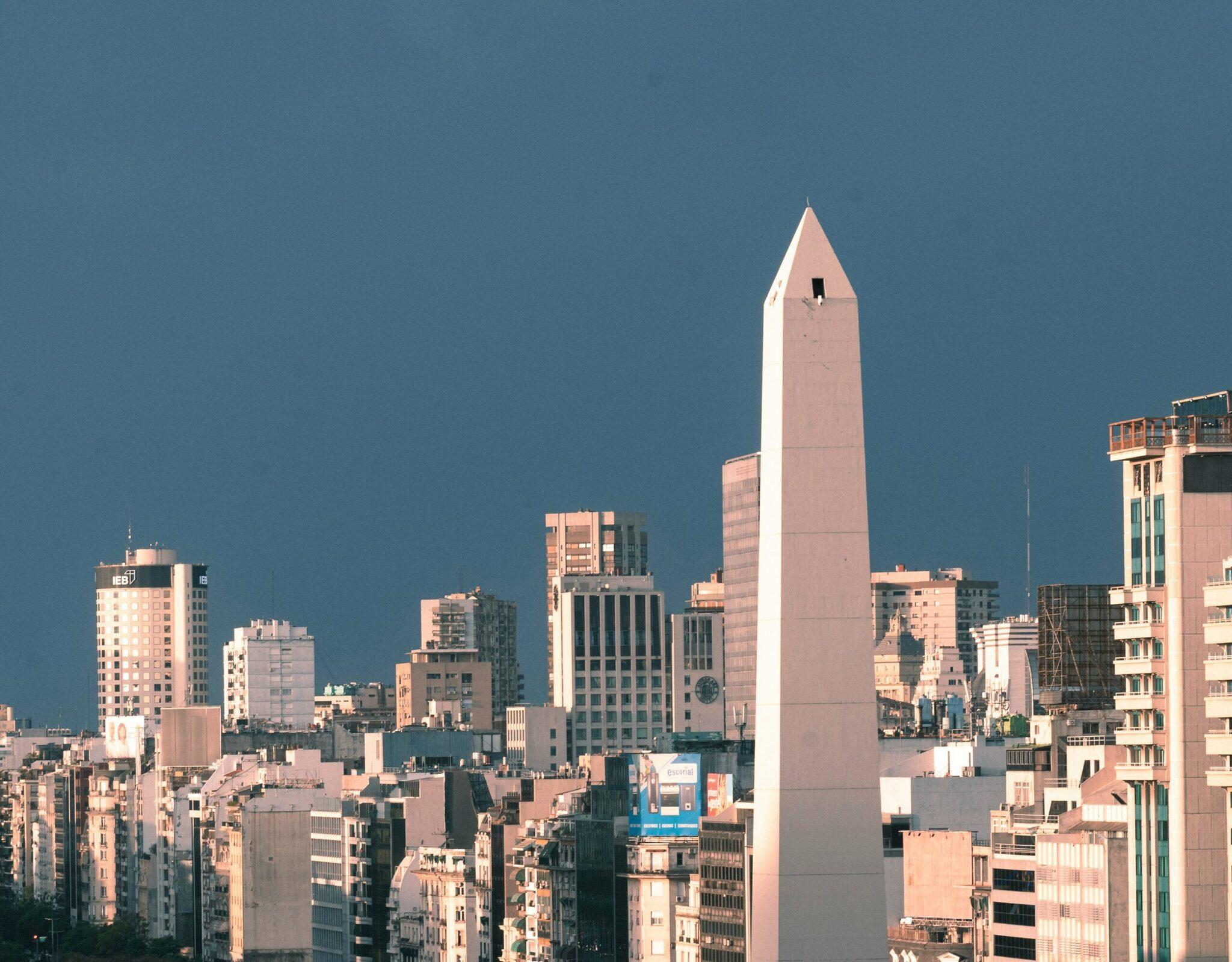 Skyline urbain avec un obélisque blanc dominant les immeubles sous un ciel bleu dégagé