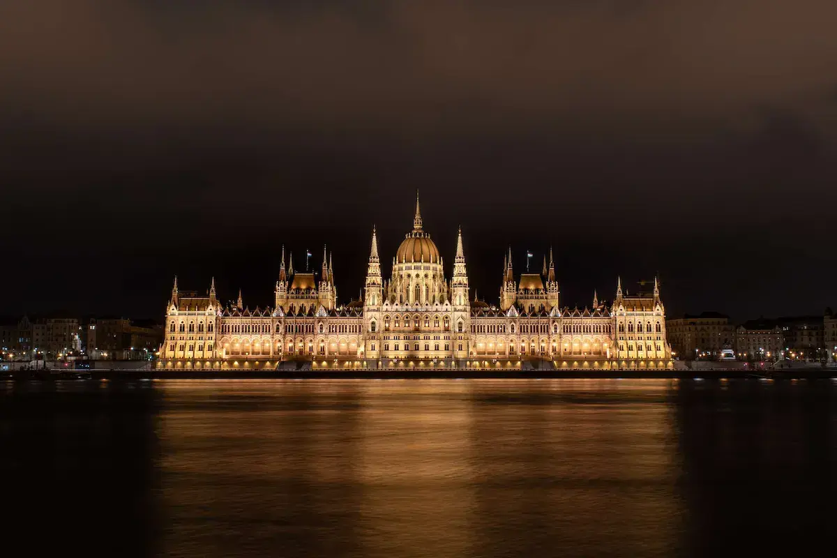 Majestueux édifice gothique illuminé la nuit bordant un fleuve aux reflets dorés