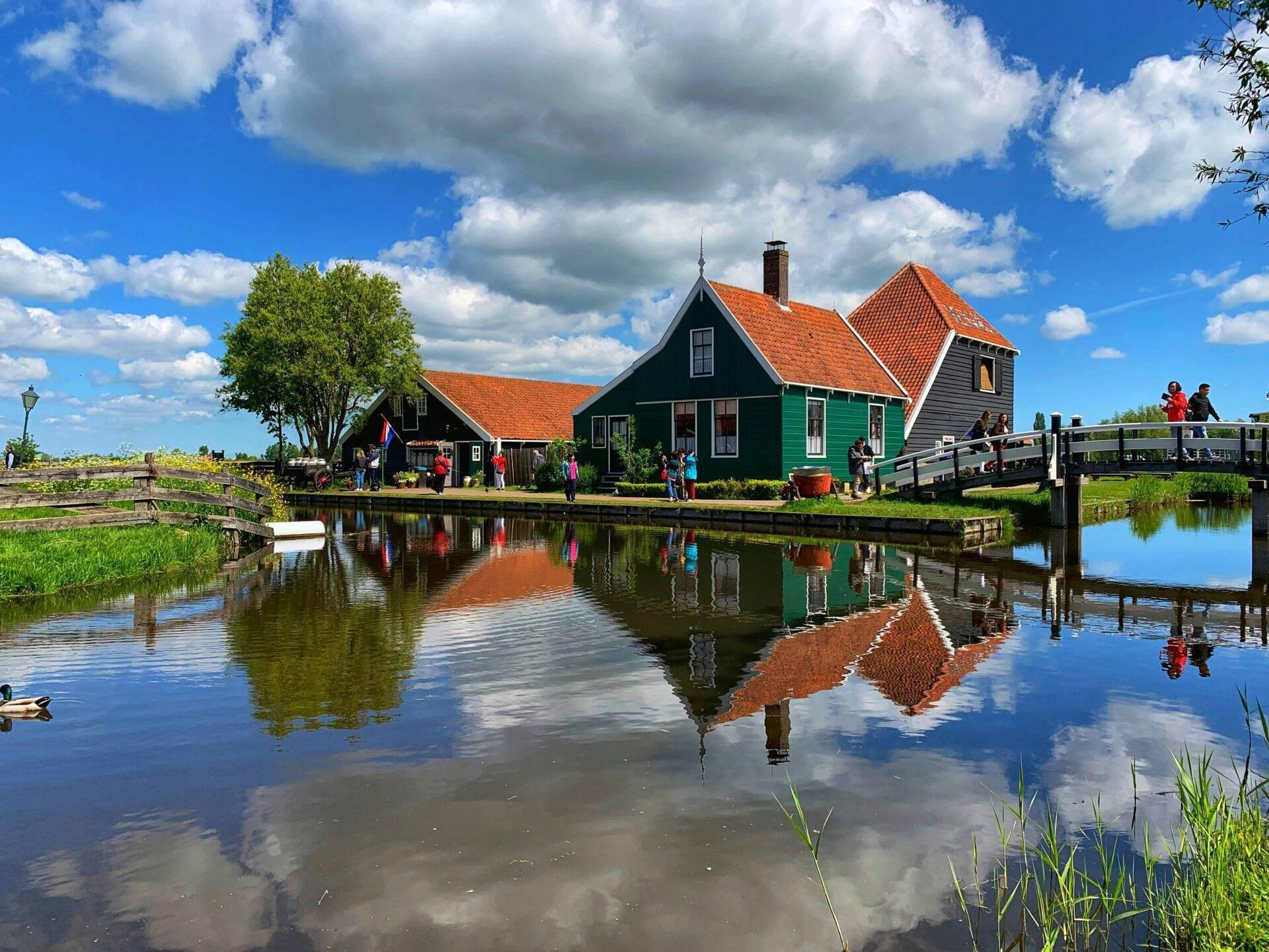 Maison traditionnelle néerlandaise aux volets verts et toit rouge, reflet dans le canal avec visiteurs et pont en bois