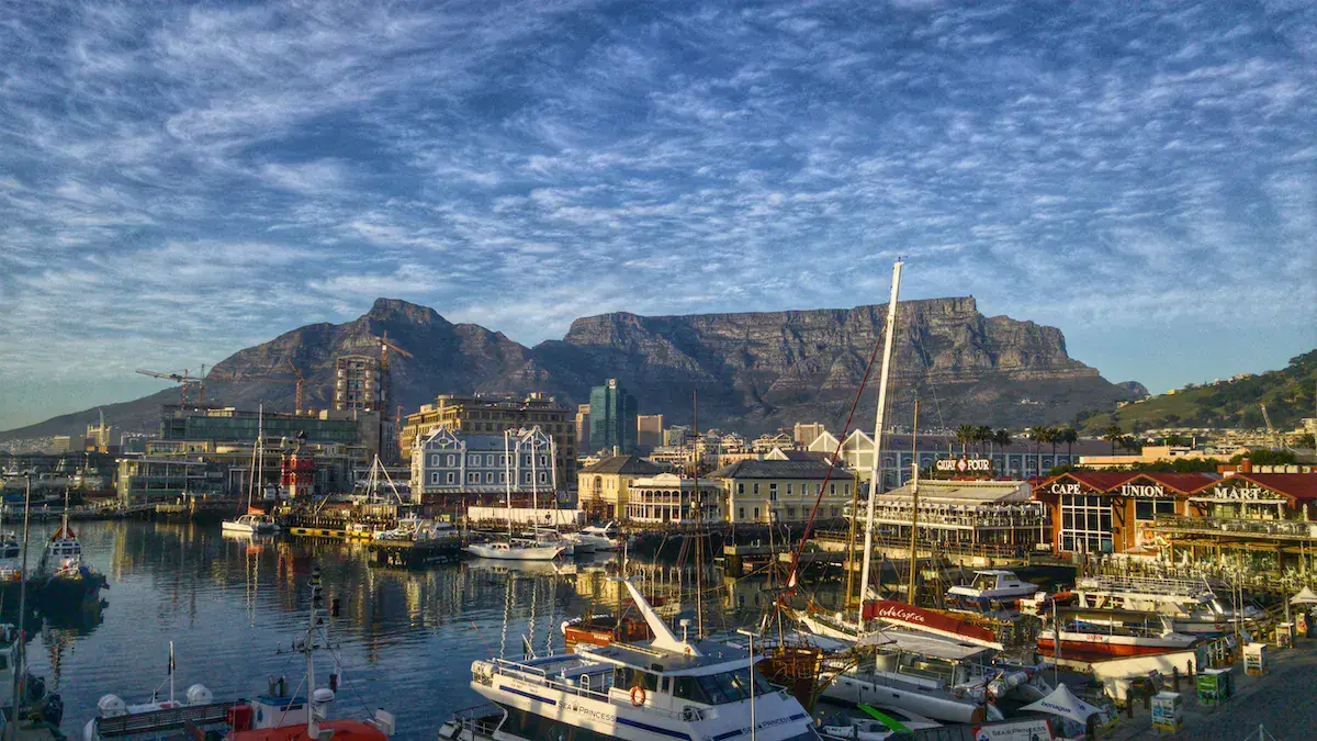Vue du port avec voiliers, bâtiments colorés et montagne distinctive en arrière-plan sous ciel bleu