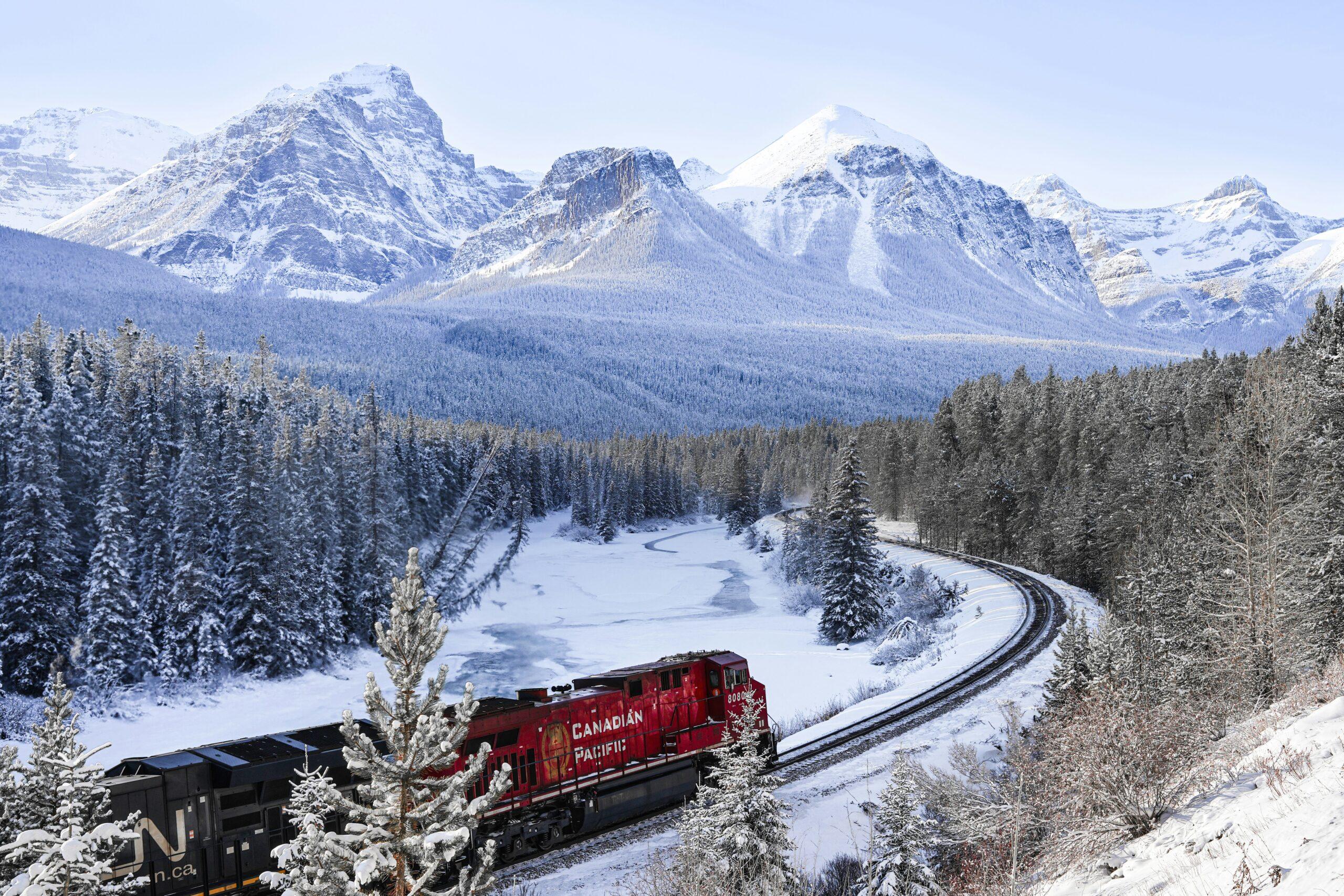 Rocky Mountaineer traversant une vallée boisée des Rocheuses canadiennes avec des sommets enneigés en arrière-plan
