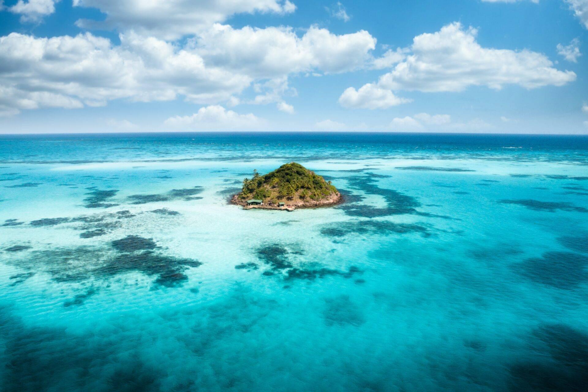 Petite île tropicale verdoyante entourée d’eaux turquoise cristallines et de récifs coralliens visibles