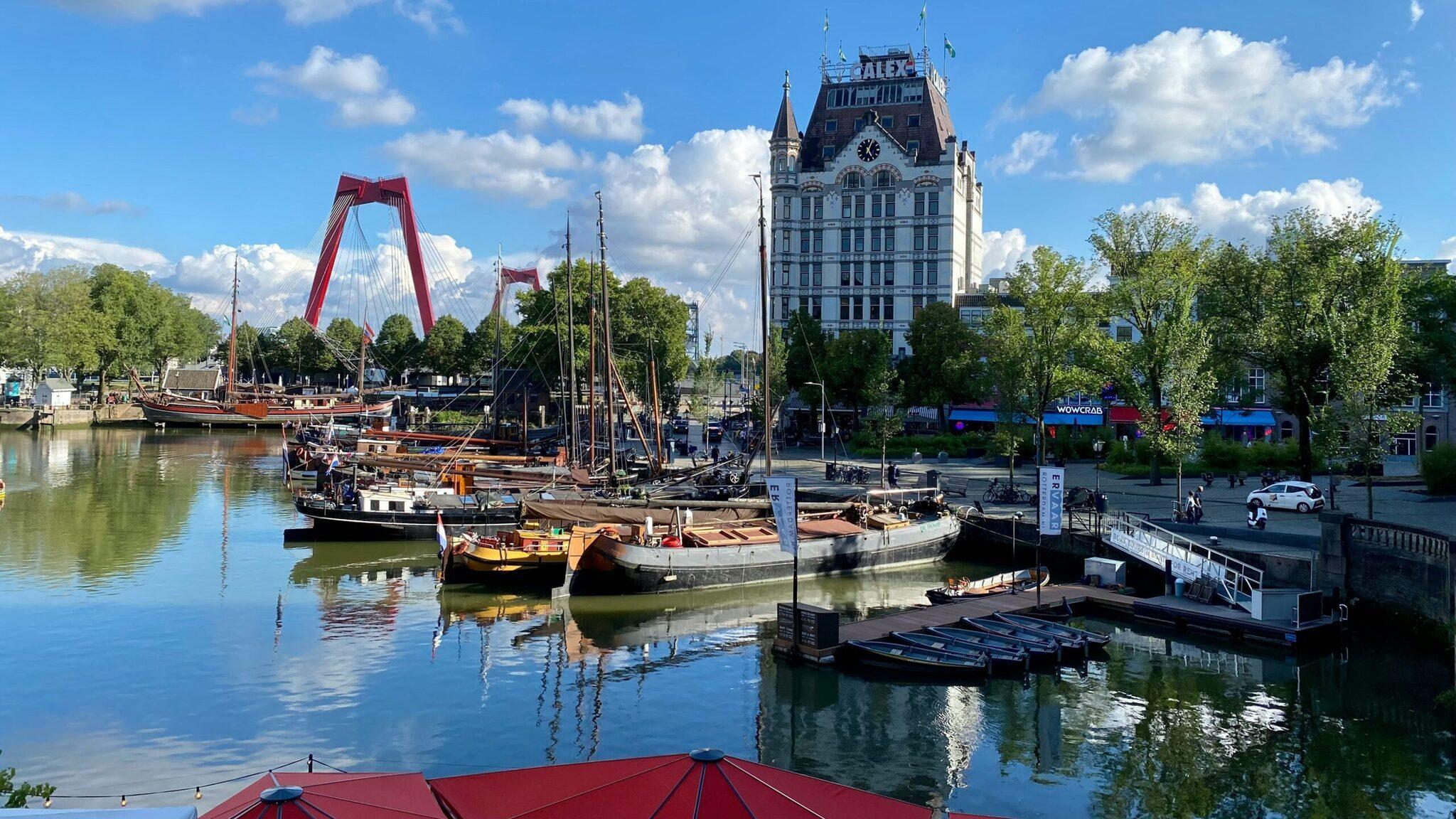 Port historique avec voiliers traditionnels, pont rouge et tour horloge dans une ville fluviale européenne