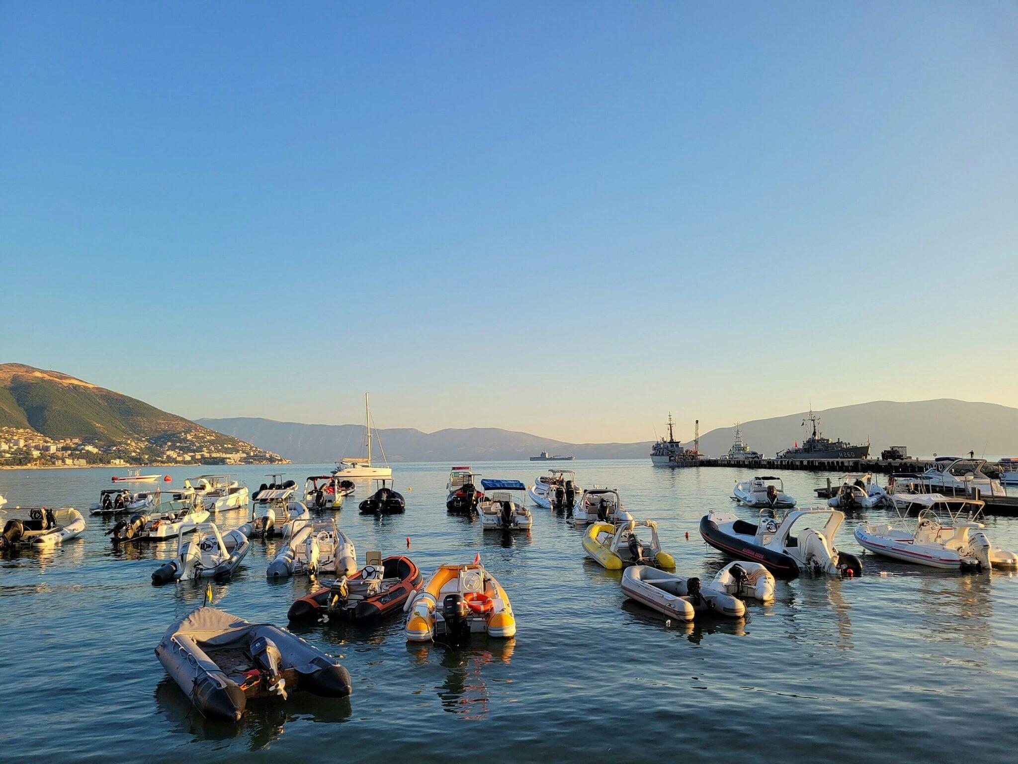 Un port méditerranéen avec des bateaux colorés ancrés dans une baie cristalline, entouré de montagnes