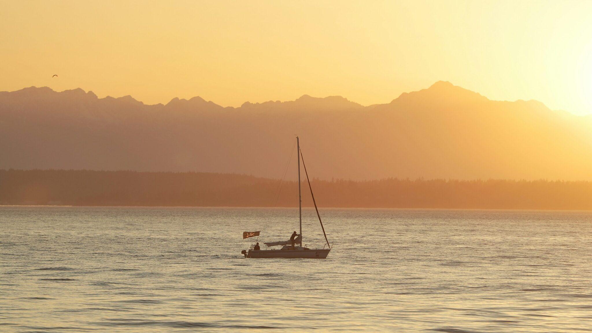 Un voilier au mouillage au coucher du soleil face à une chaîne de montagnes enneigées en arrière-plan
