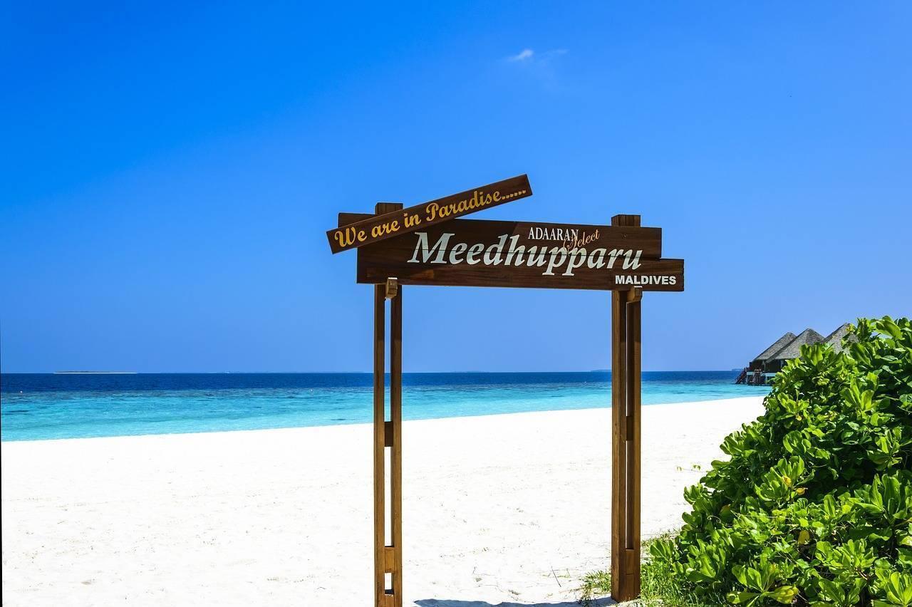 Panneau en bois “We are in Paradise” sur une plage de sable blanc avec lagon turquoise aux Maldives