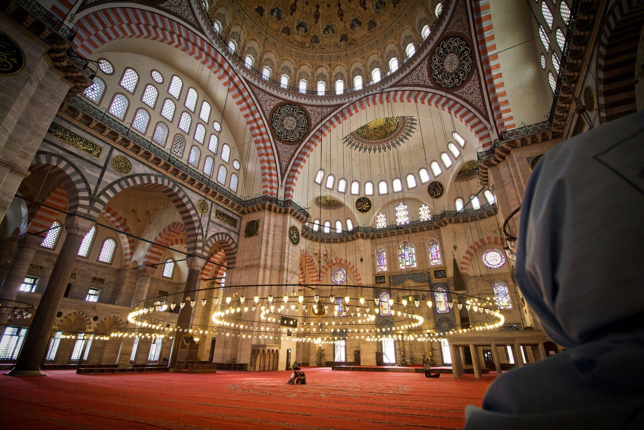 Intérieur majestueux d’une mosquée avec dôme, lustres dorés et colonnes à arcs rouges et blancs