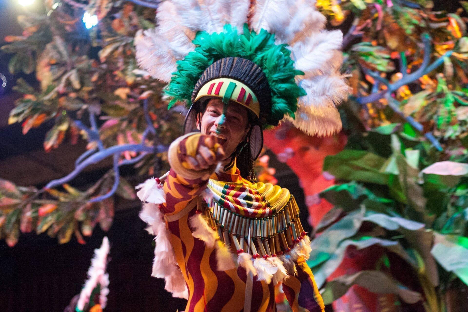 Un danseur en costume traditionnel coloré avec coiffe à plumes vertes lors d’une parade festive brésilienne