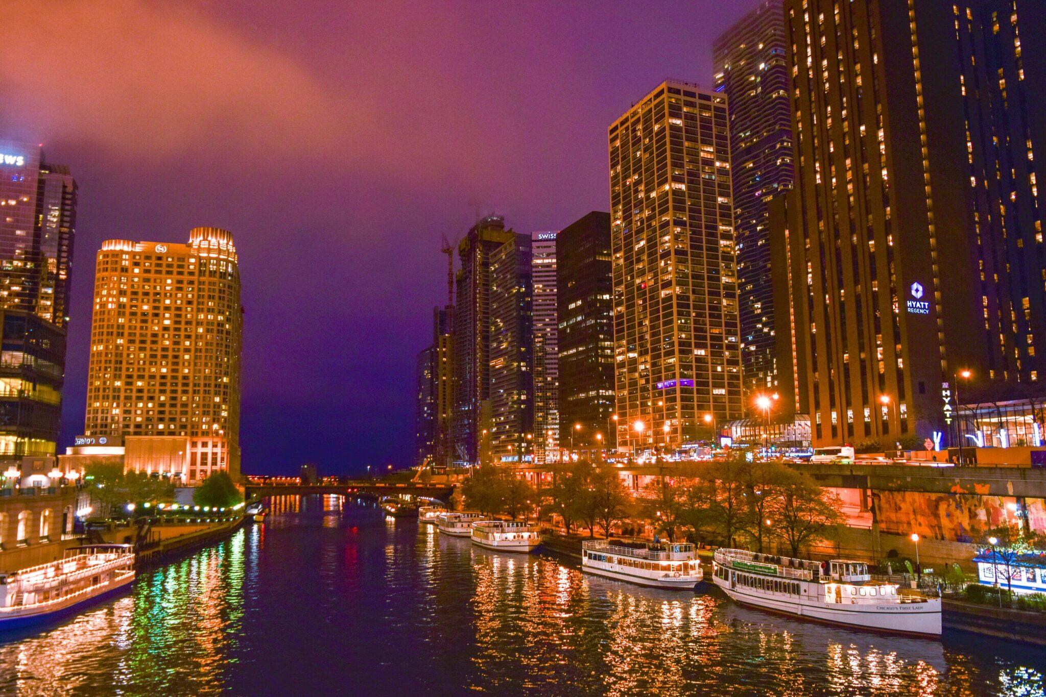 Vue nocturne d’une rivière urbaine bordée de gratte-ciel illuminés et de bateaux de croisière