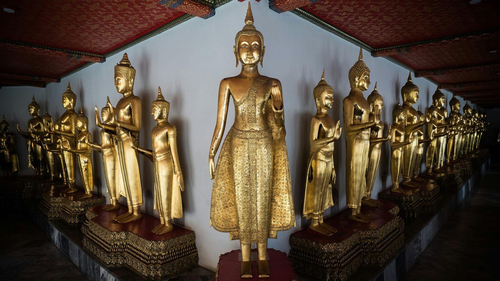 Galerie intérieure d’un temple thaïlandais avec une statue de Bouddha centrale dorée entourée de rangées de statues dorées