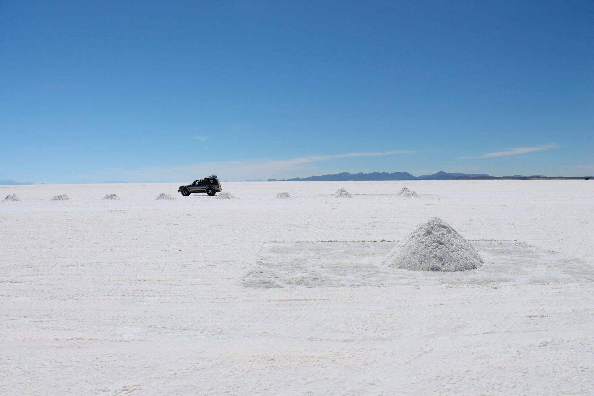 Un véhicule tout-terrain noir traverse un vaste désert de sel blanc avec monticules de minéraux et montagnes lointaines