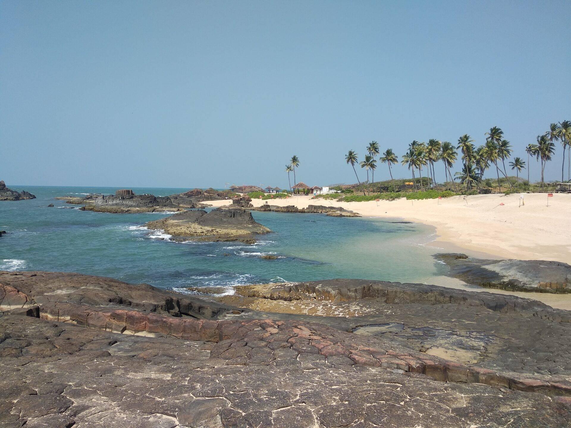 Vue côtière avec plage de sable blanc, rochers volcaniques, cocotiers et petits îlots rocheux en mer turquoise