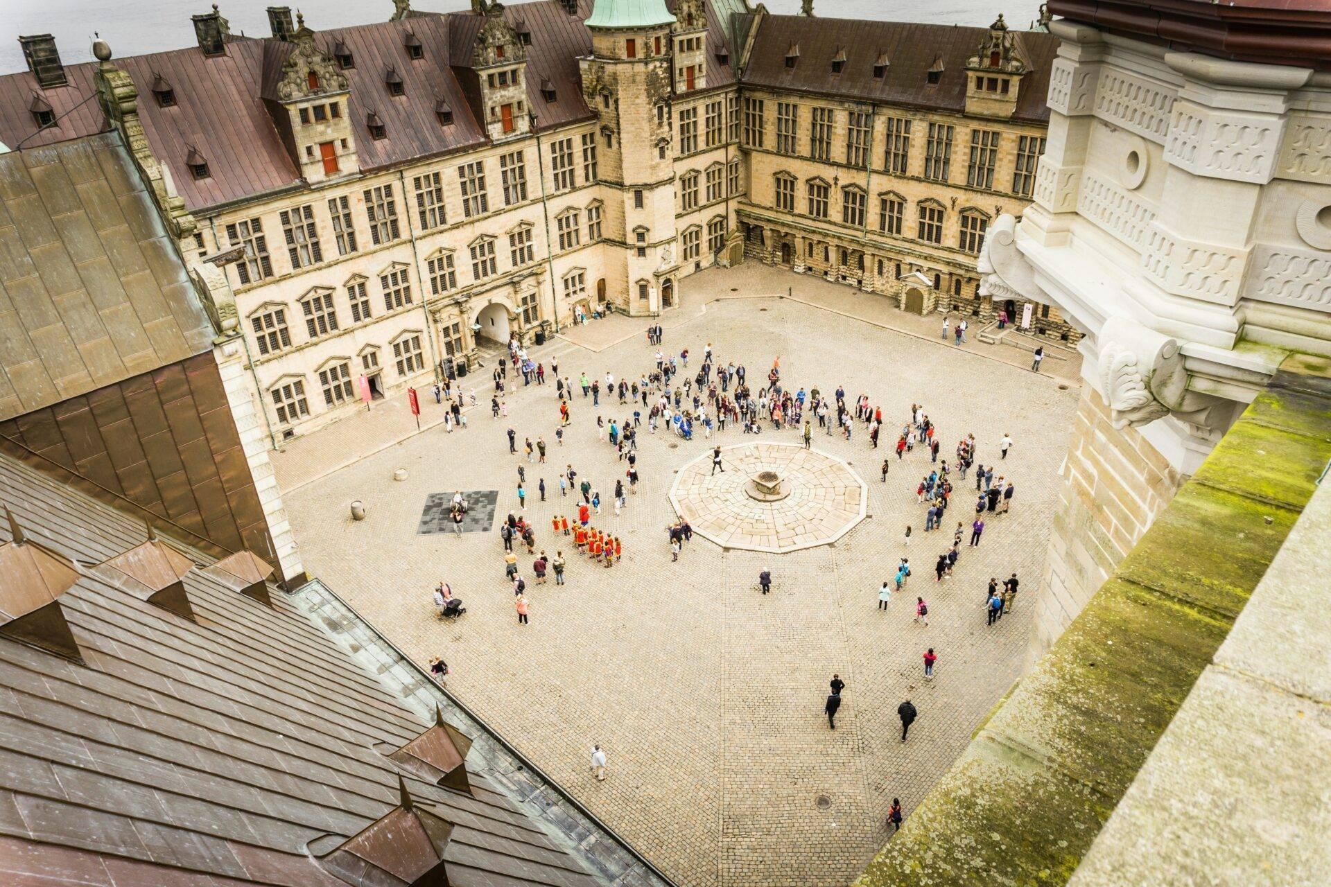 Vue aérienne d’une cour intérieure de château médiéval avec touristes, bâtiments en pierre et toits en cuivre
