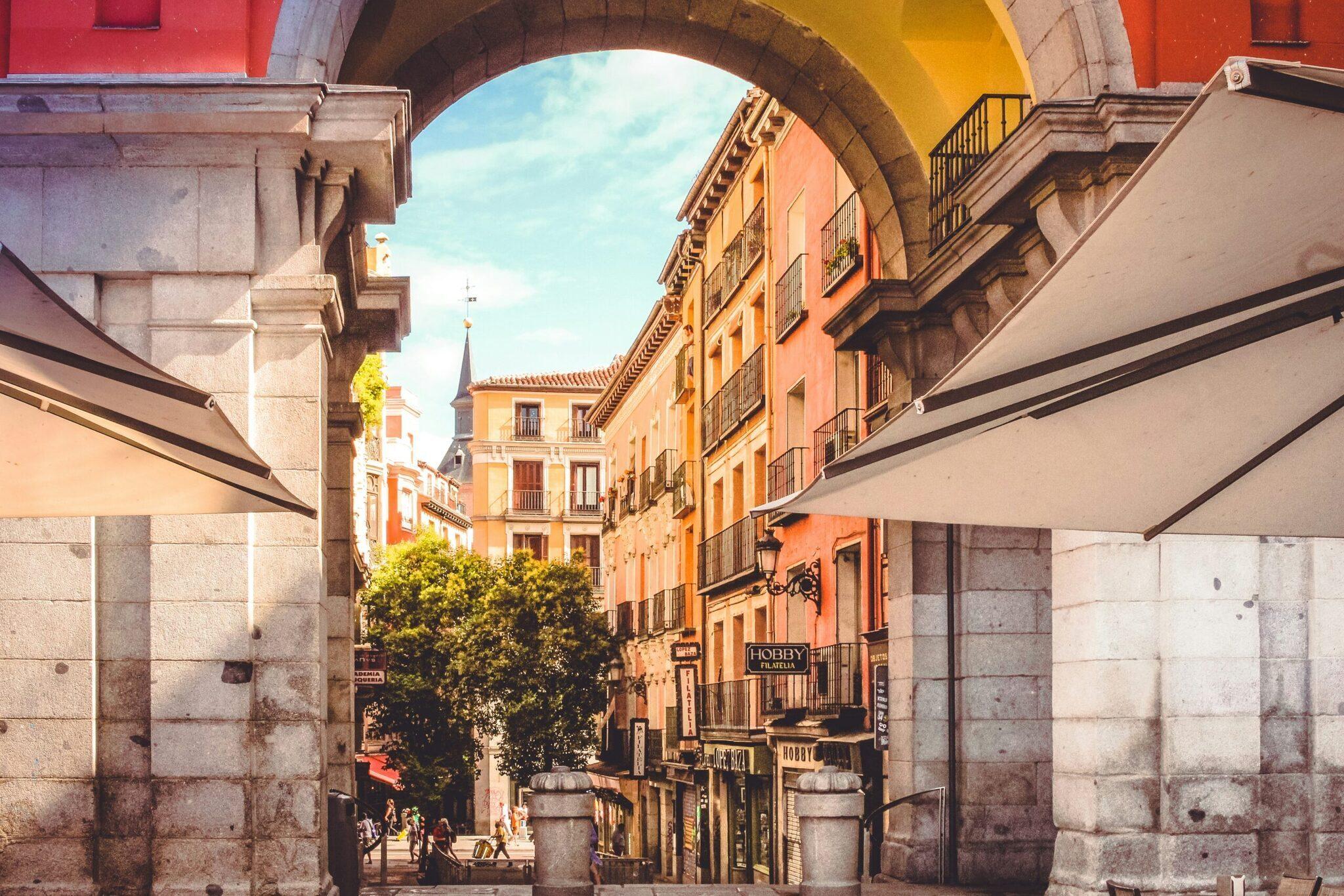 Une rue historique de Madrid encadrée par des bâtiments orangés et ocre avec arcades, signalétique commerciale et ciel dégagé