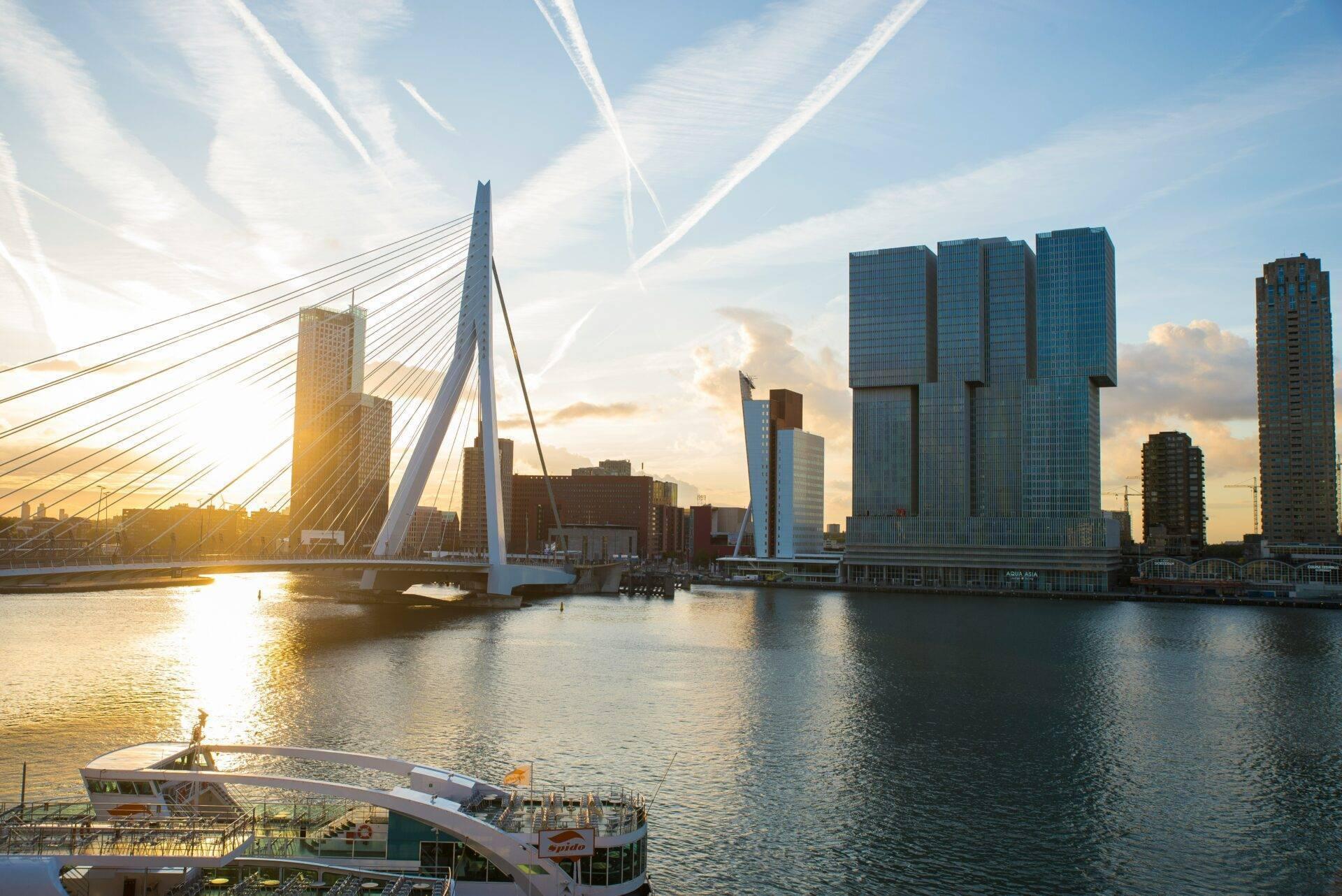 Un pont blanc moderne enjambant un canal avec gratte-ciel et bateaux au coucher de soleil