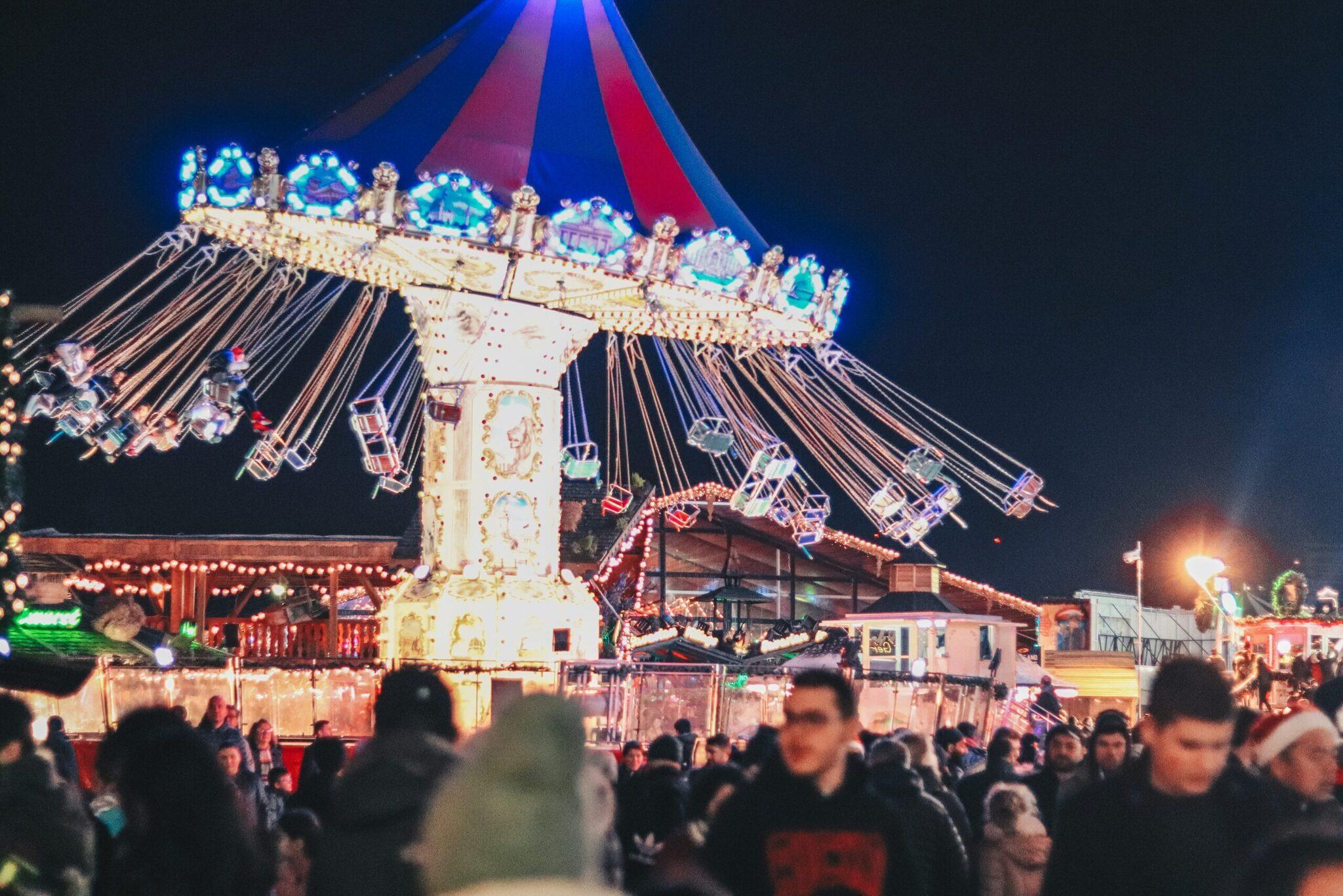 Un manège illuminé de nuit dans un marché de Noël avec foule de visiteurs et décoration festive colorée