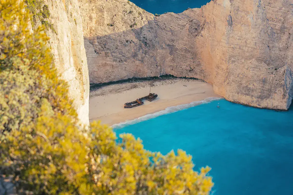 Vue aérienne d’une baie encaissée aux falaises blanches avec plage de sable, eau turquoise et épave de navire échouée