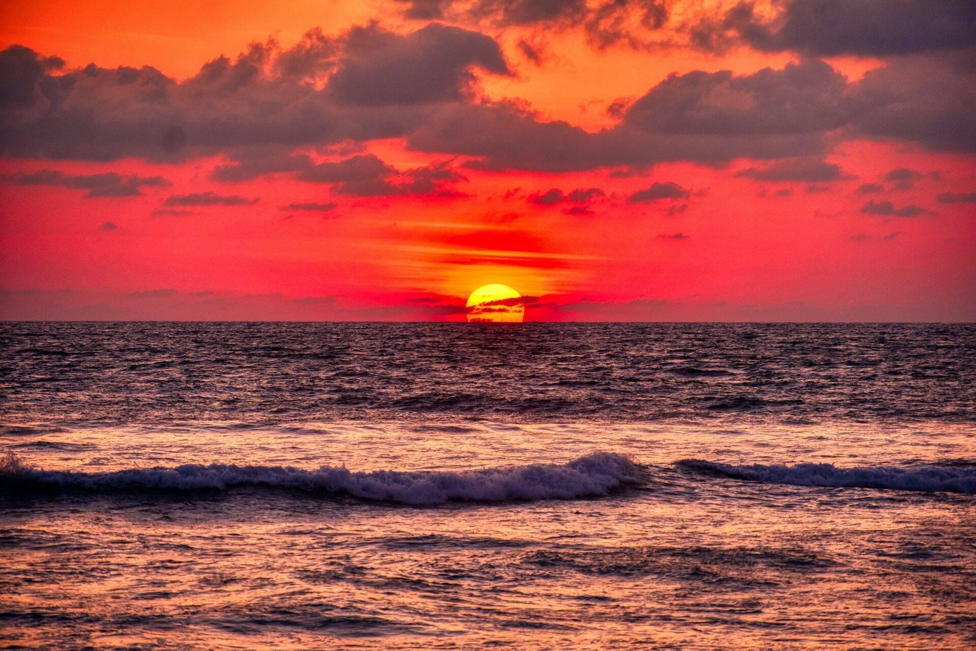 Coucher de soleil flamboyant sur l’océan avec vagues et ciel rouge orangé spectaculaire