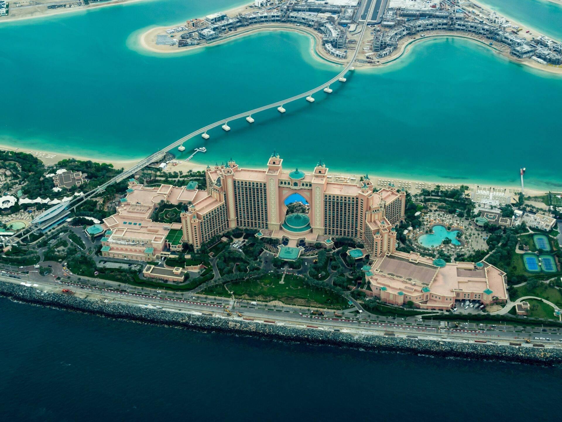 Vue aérienne d’un luxueux resort balnéaire avec architecture dorée, piscines turquoise et plage privée aux Émirats arabes