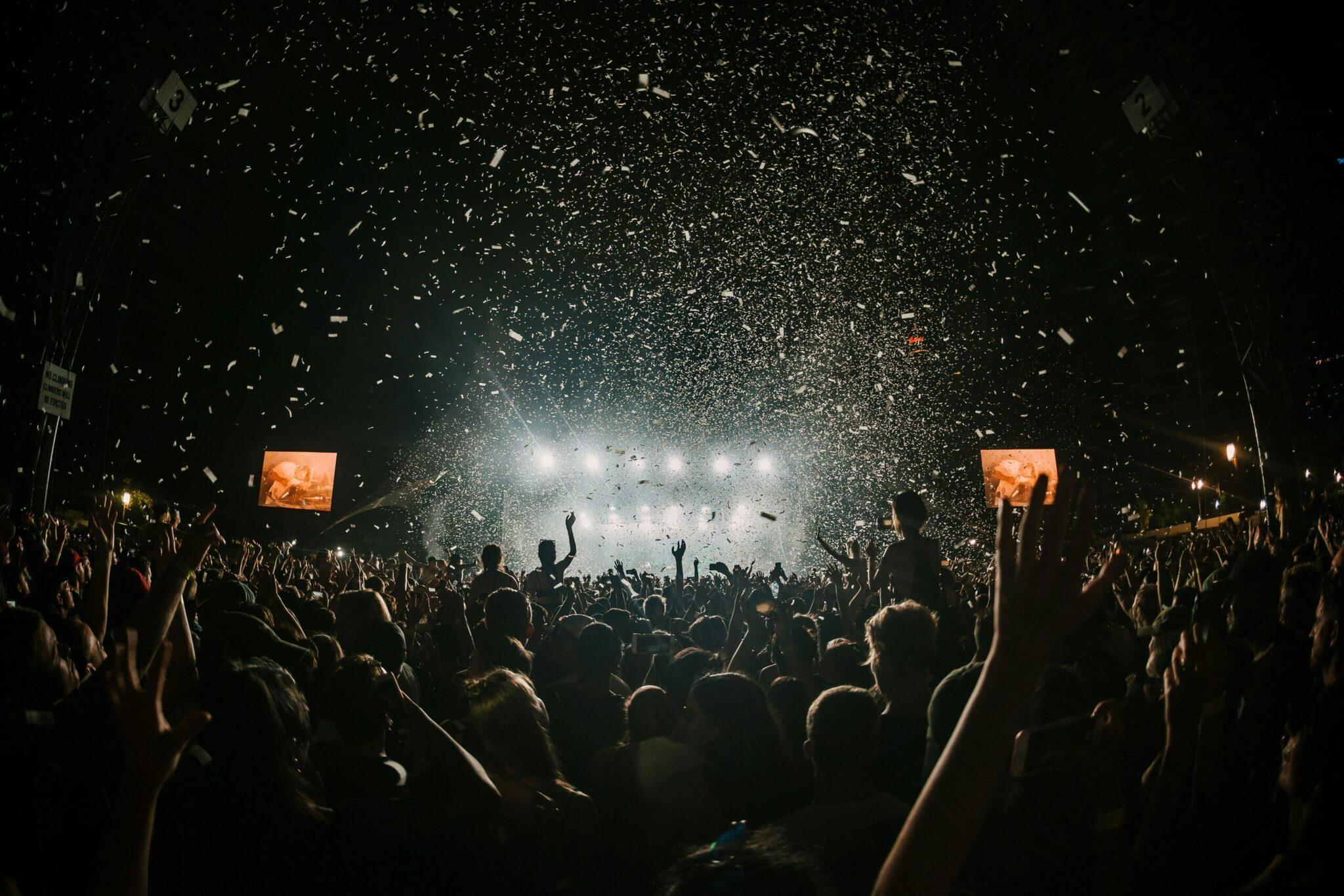 Foule en liesse lors d’un concert de nuit avec confettis tombant sous les projecteurs et écrans géants