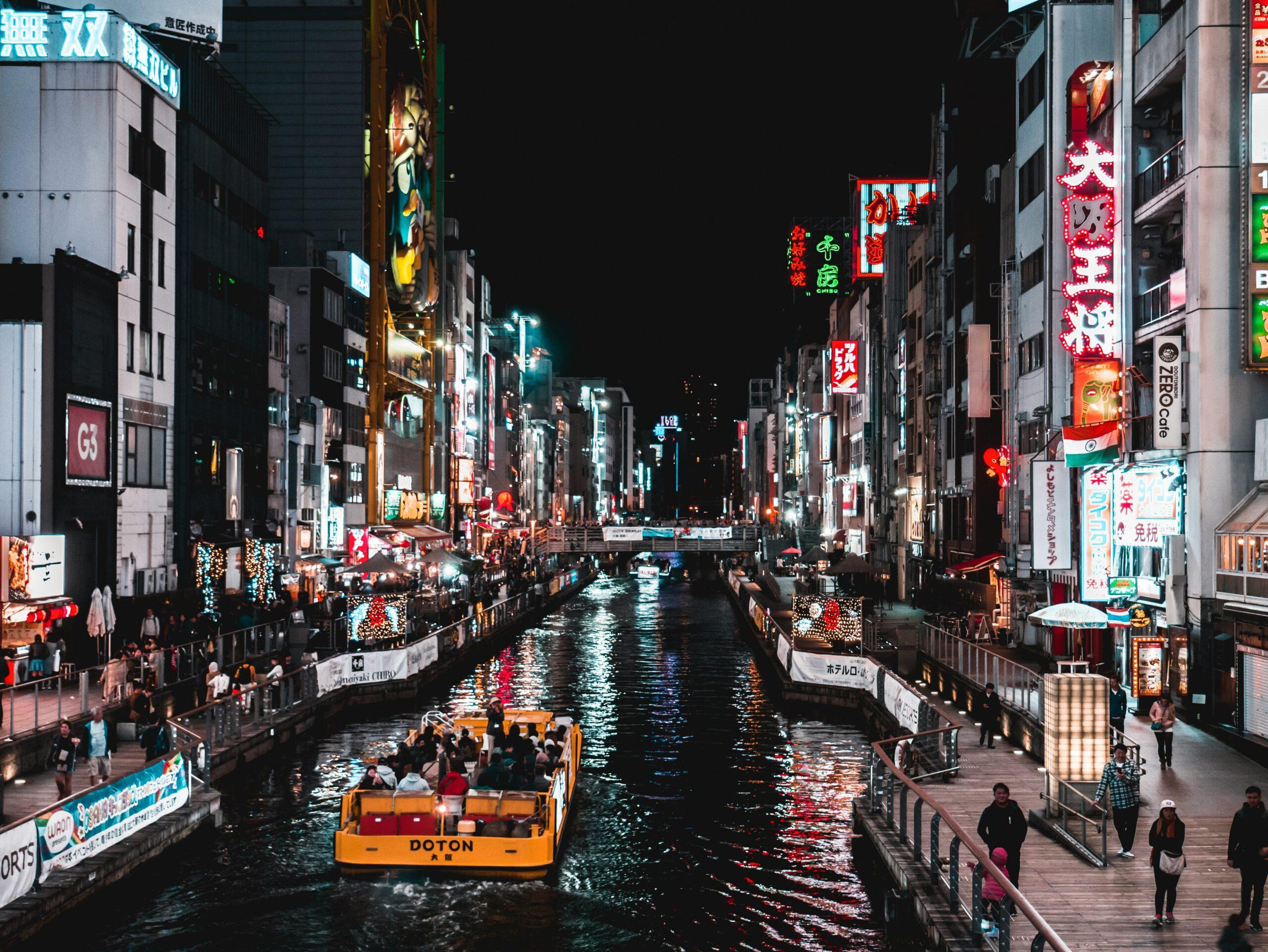 Un canal illuminé de nuit dans une rue commerçante japonaise animée avec néons et bateau touristique jaune