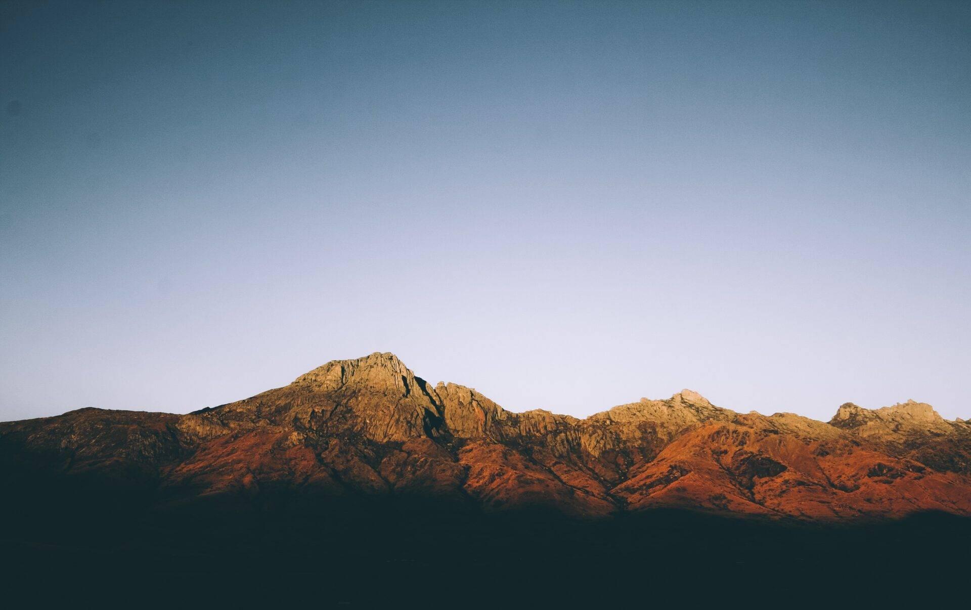 Une chaîne de montagnes rocheuses aux teintes ocre et rougeâtre illuminées par le soleil couchant sous un ciel dégagé