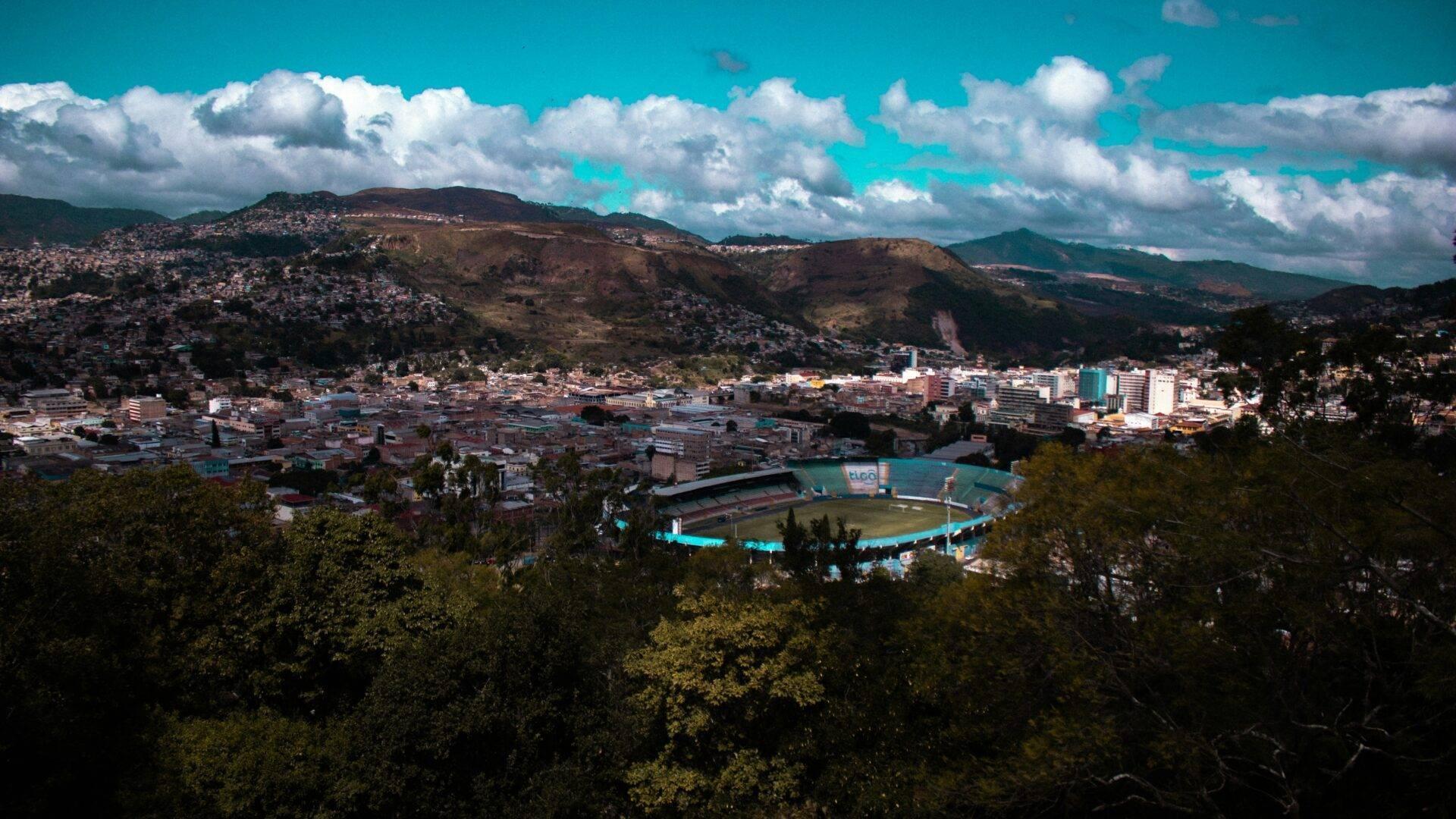 Vue panoramique d’une ville de montagne avec un stade bleu turquoise, entourée de collines boisées et de bâtiments résidentiels