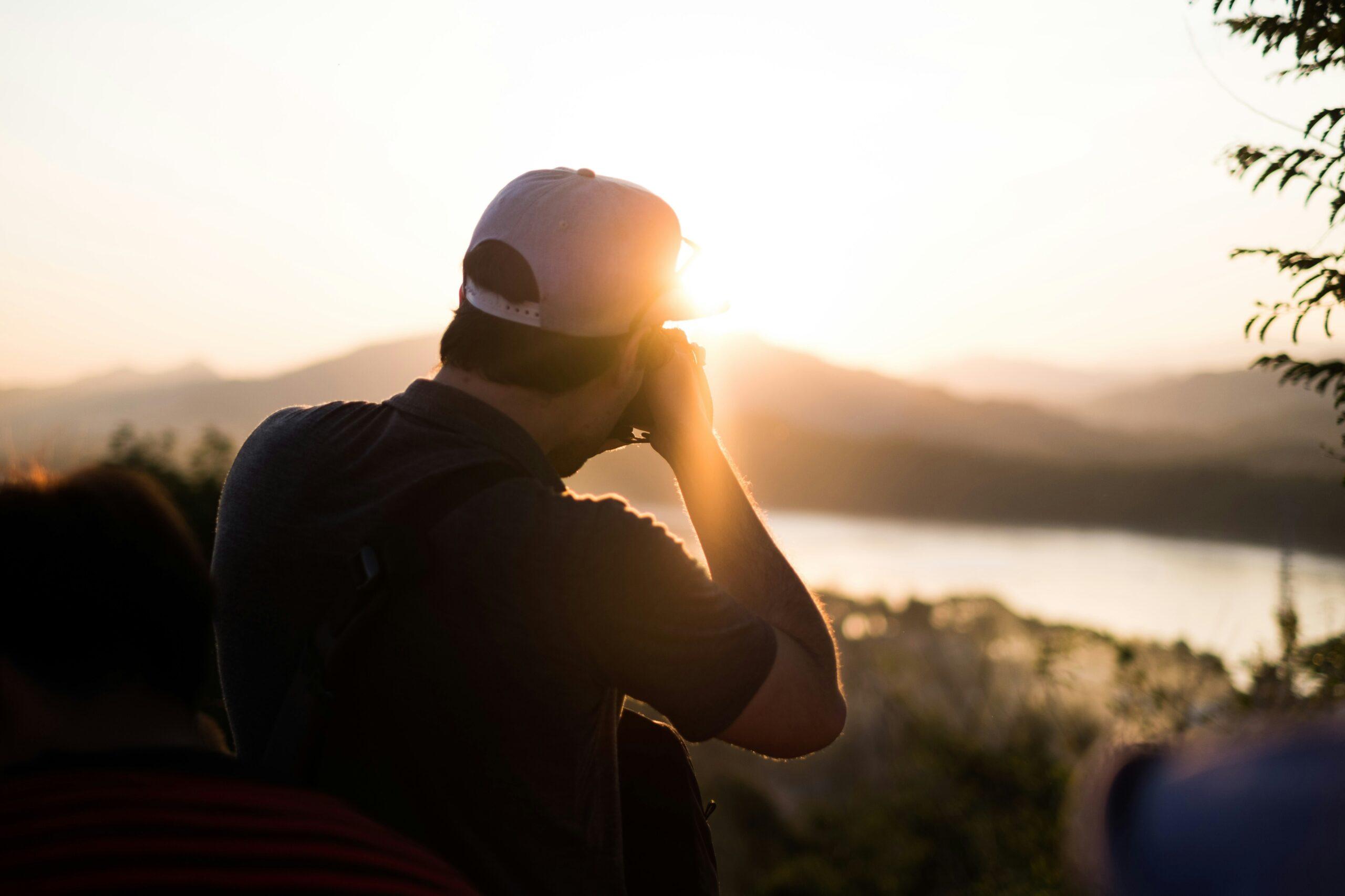 Homme au coucher de soleil observant un paysage montagneux avec un lac depuis un point de vue panoramique