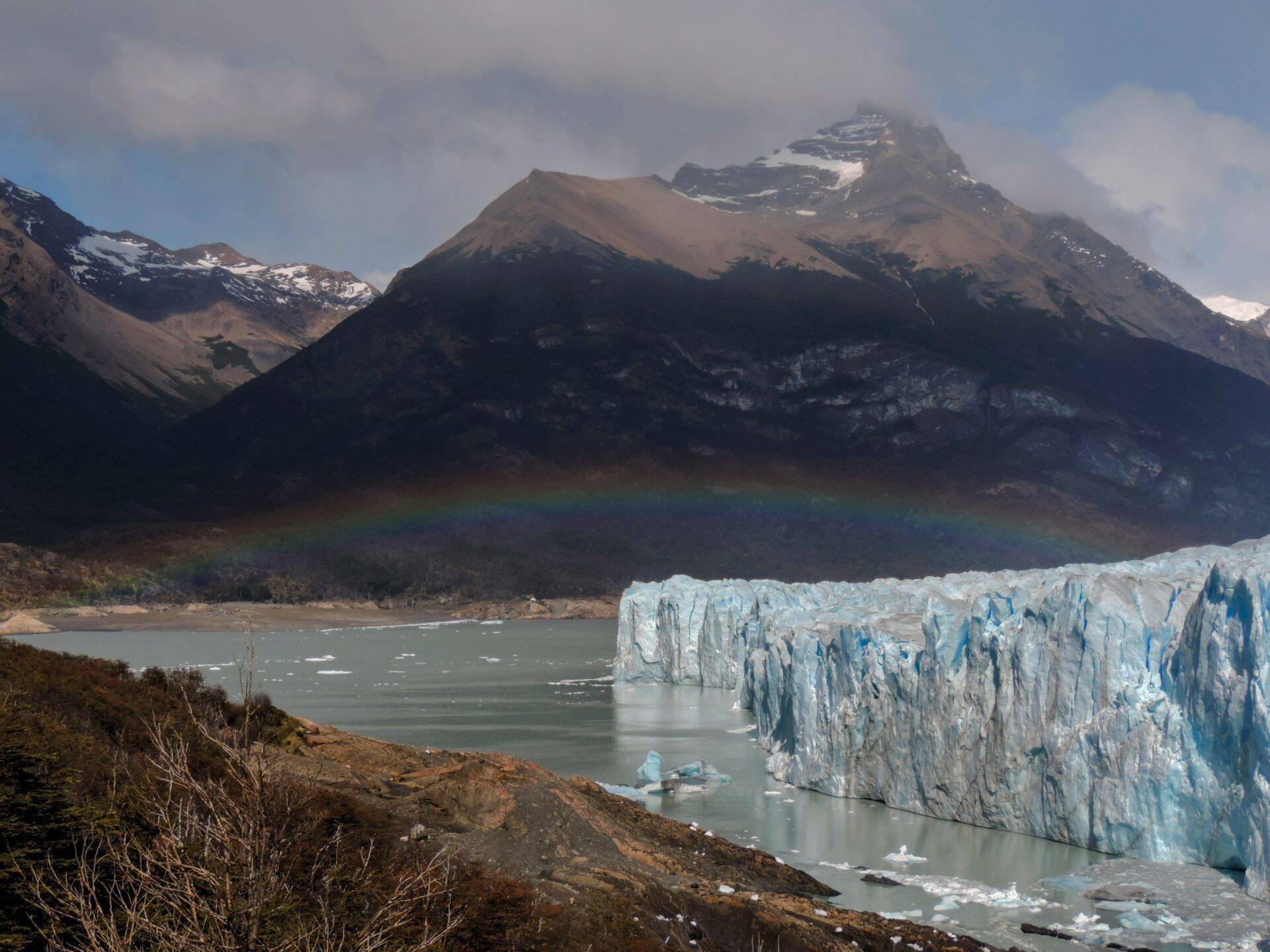 Glacier blanc face à une montagne enneigée se reflétant dans un lac glaciaire turquoise avec arc-en-ciel