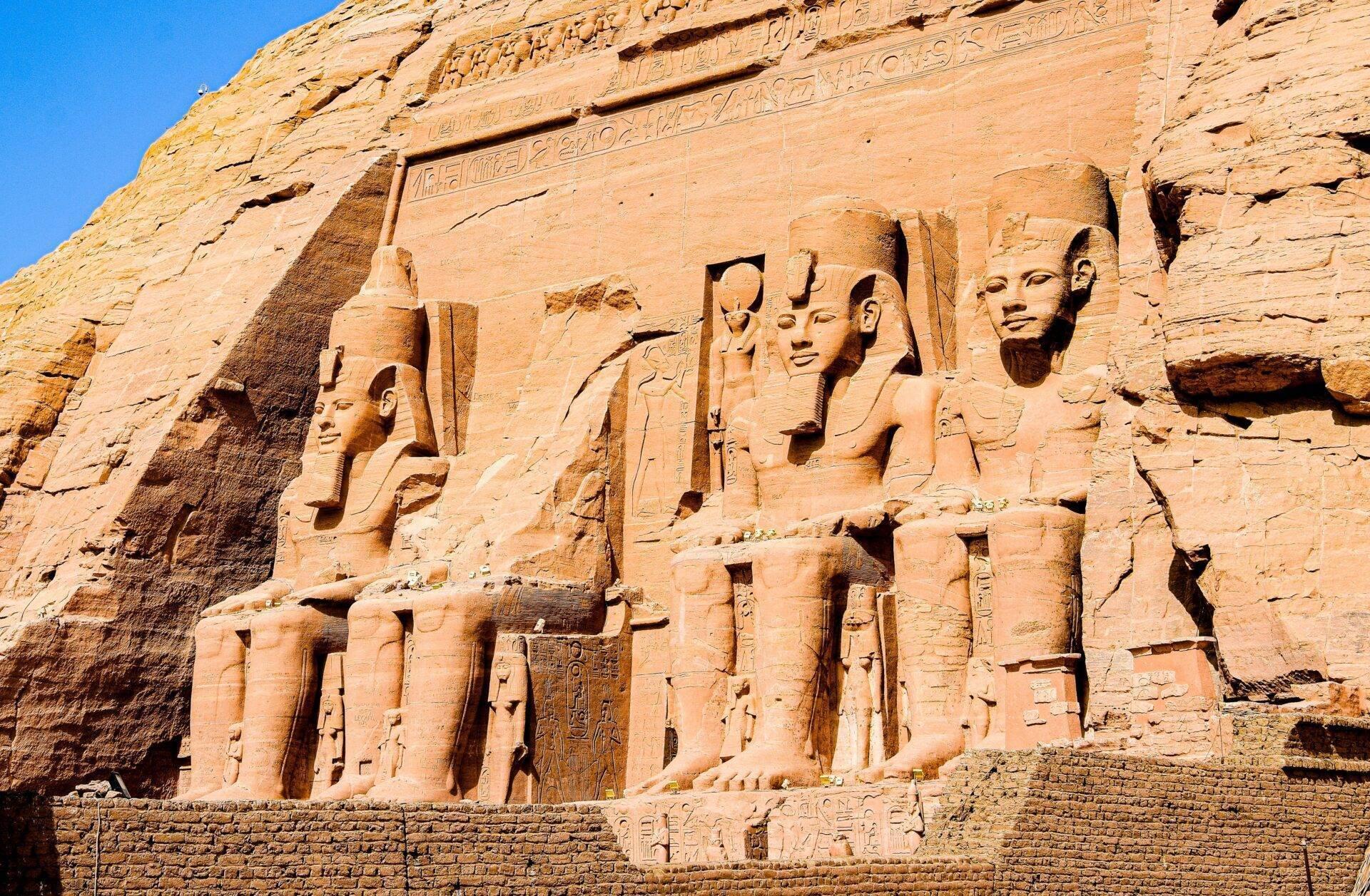 Façade rocheuse d’un temple égyptien antique avec quatre colosses sculptés et hiéroglyphes sous ciel bleu