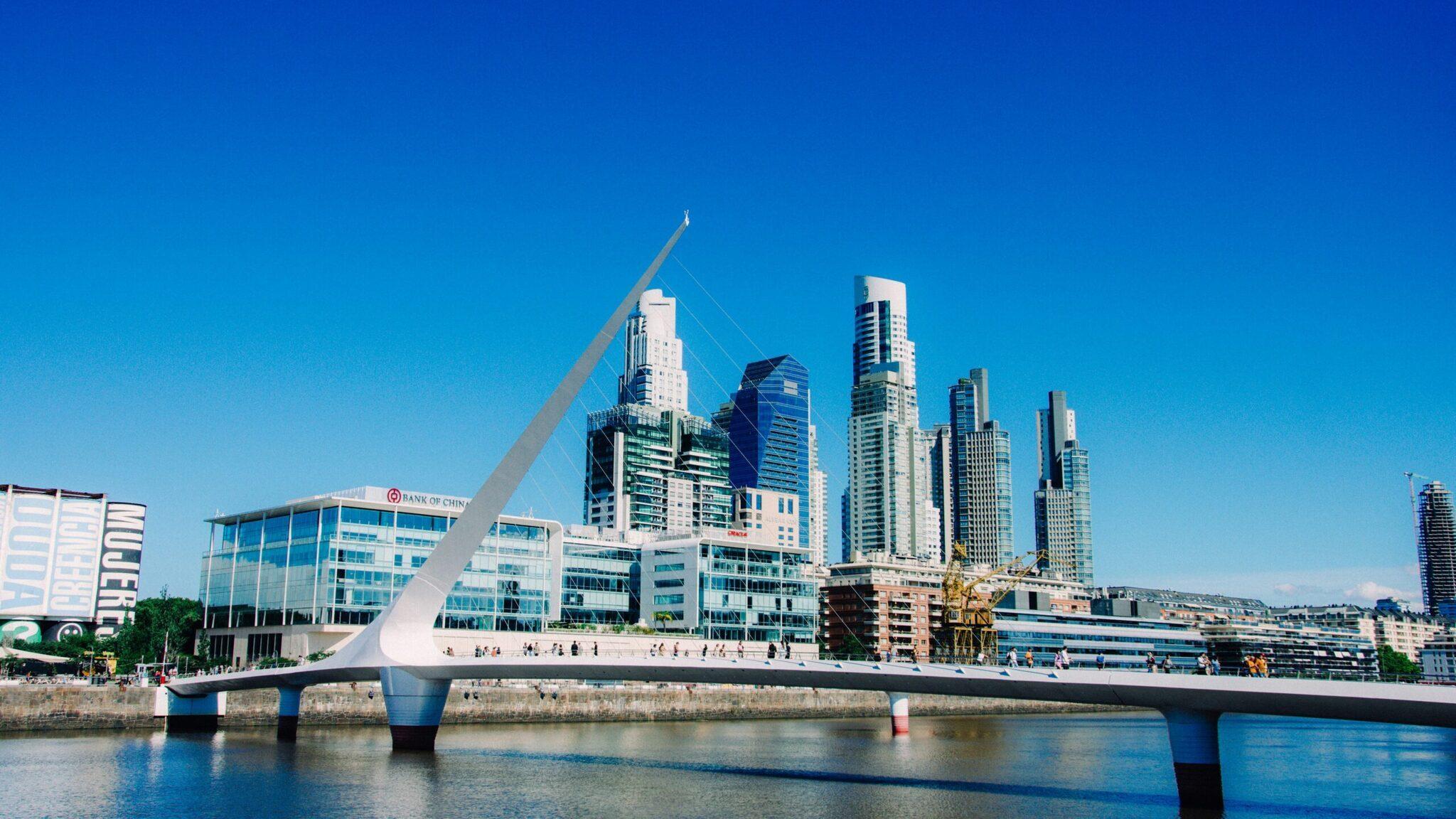 Un pont blanc moderne enjambant un fleuve avec des gratte-ciel contemporains en arrière-plan sous un ciel bleu dégagé