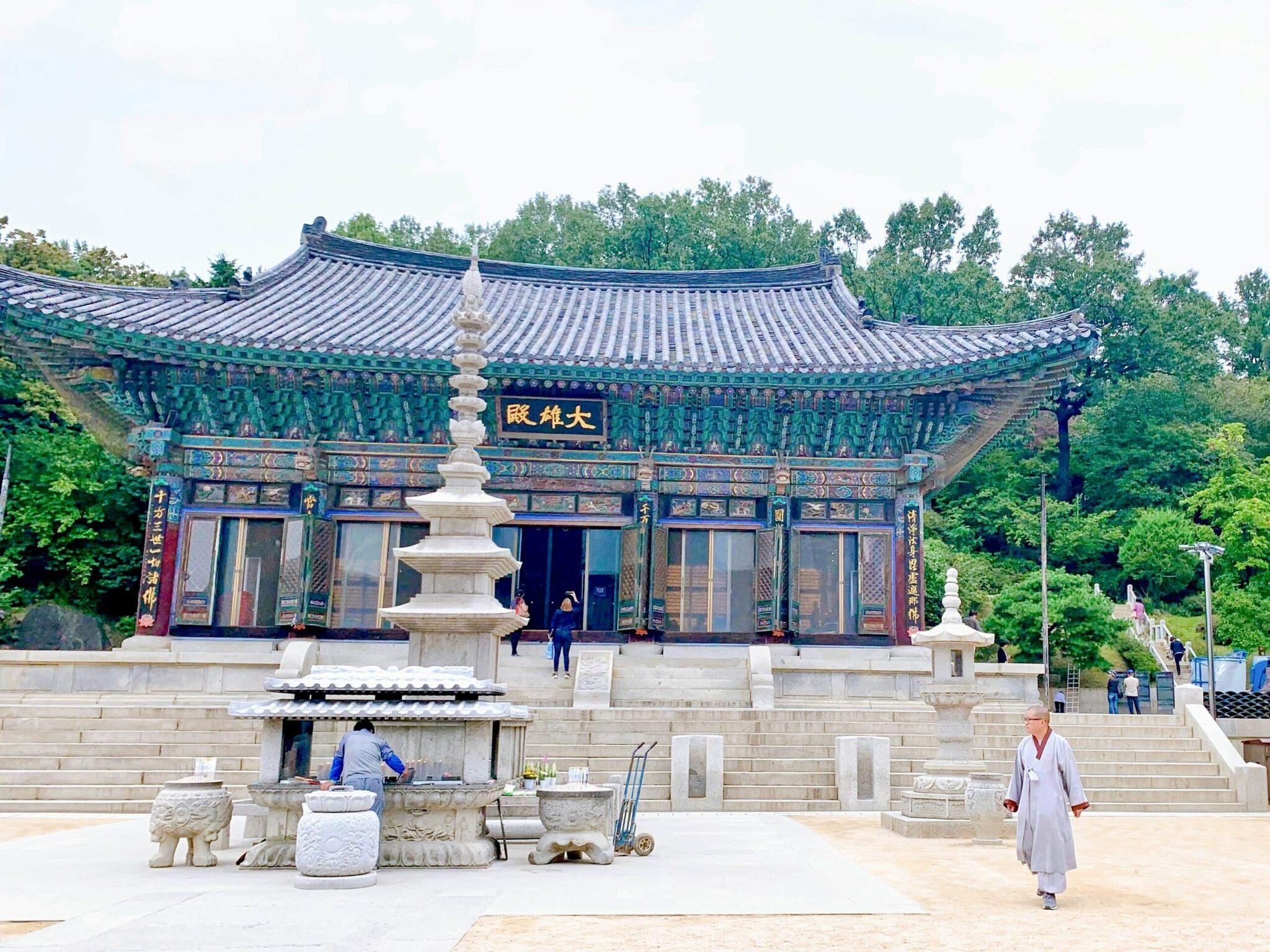 Un temple bouddhiste coréen avec toiture traditionnelle bleue et verte, stupa en pierre, et visiteurs dans une cour pavée