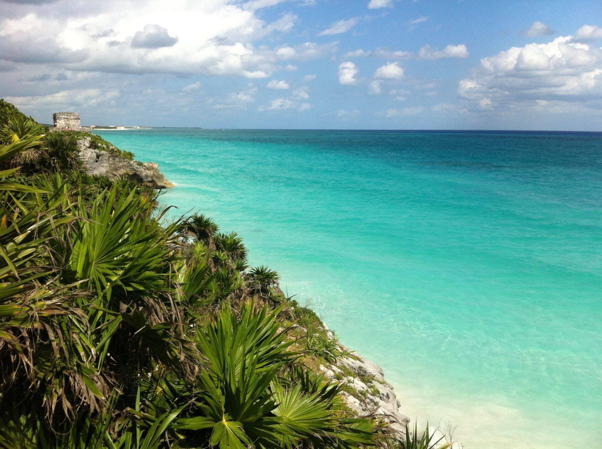 Ruine maya sur une falaise rocheuse dominant une mer turquoise cristalline bordée de végétation tropicale