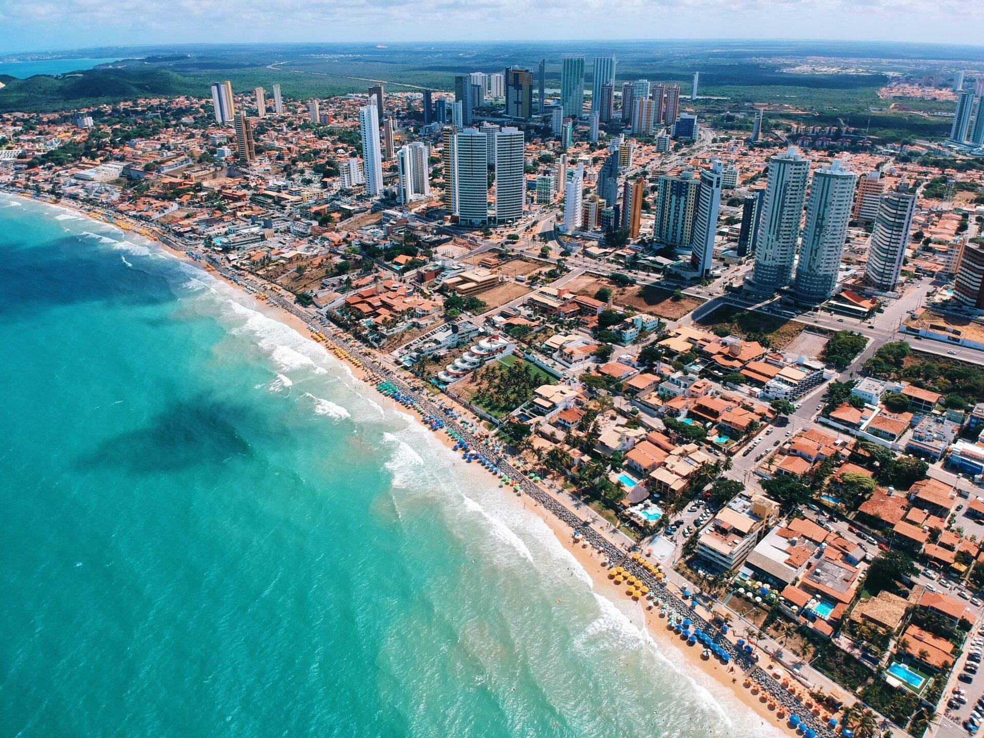 Vue aérienne d’une station balnéaire côtière avec plage turquoise, gratte-ciel modernes et résidences colorées au bord de mer
