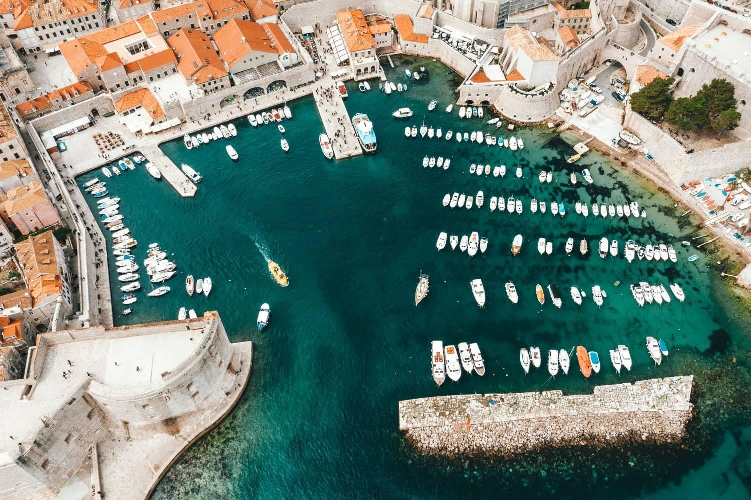 Vue aérienne d’un port méditerranéen pittoresque avec voiliers blancs amarrés dans une baie turquoise entourée d’architecture historique
