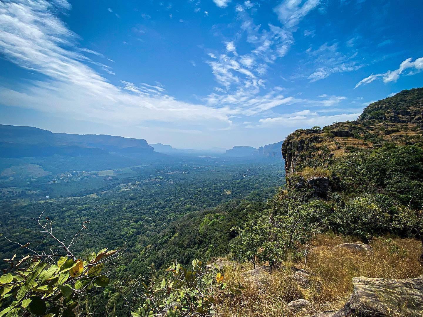 Vue panoramique depuis un plateau rocheux sur une vallée verdoyante avec formations montagneuses en arrière-plan sous ciel bleu