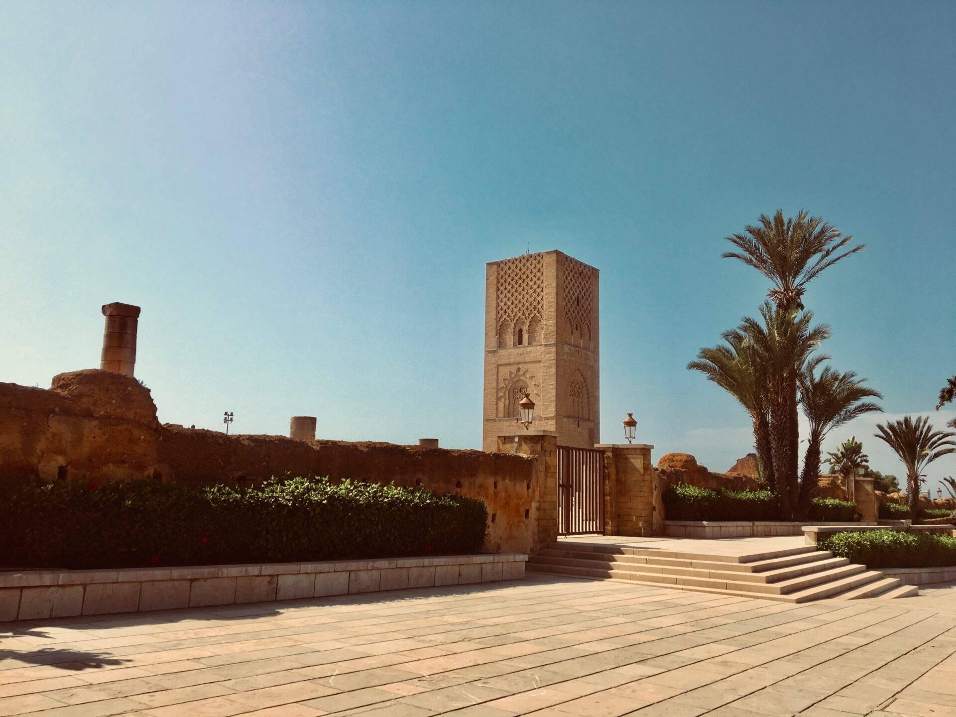 Une mosquée traditionnelle marocaine avec minaret en terre cuite, terrasse pavée et palmiers sous ciel bleu