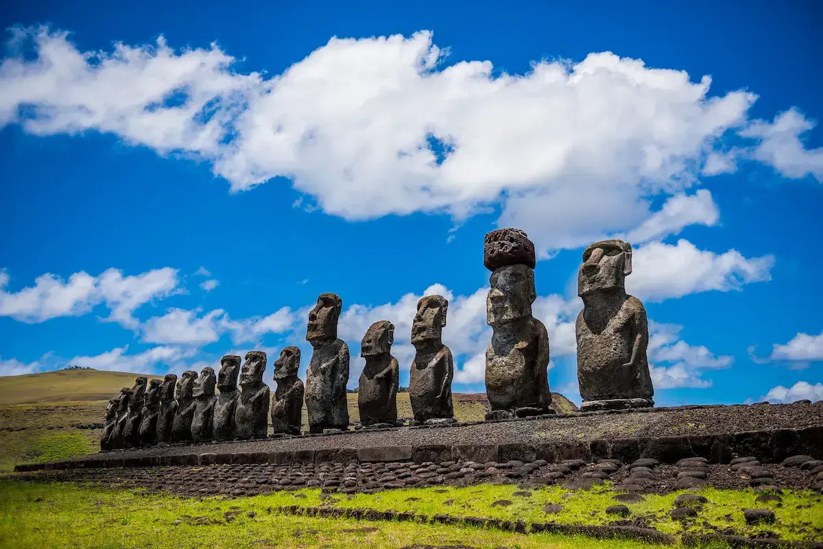 Une rangée de moaïs géants en pierre sur un plateau herbeux sous un ciel bleu dégagé
